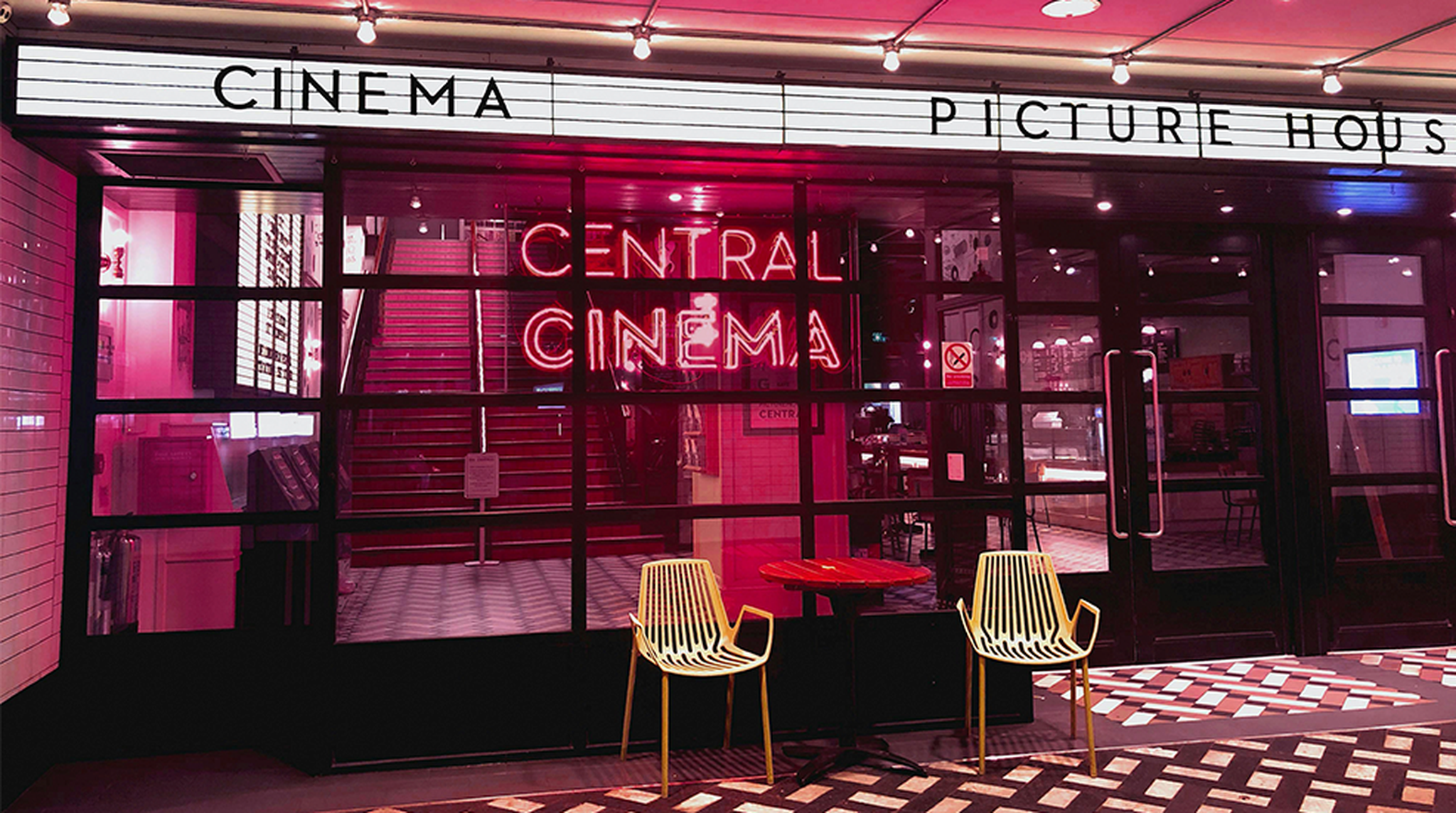 Entrance to "Central Cinema" with neon sign, two yellow chairs, and a red table outside. Marquee above reads "Cinema Picture House."