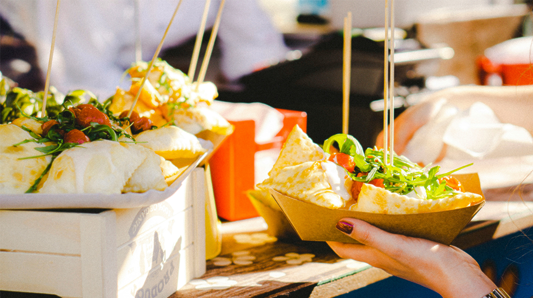 Close up of a woman's hand holding a cardboard takeaway bowl of food from a market stool