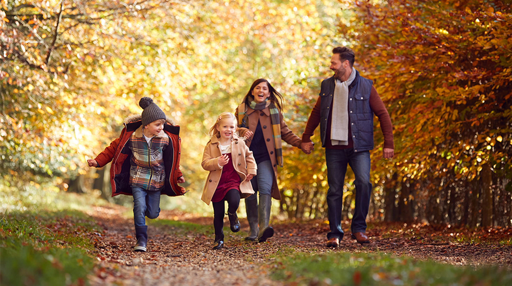Family Walking Along Track In Autumn Countryside With Children Running Ahead