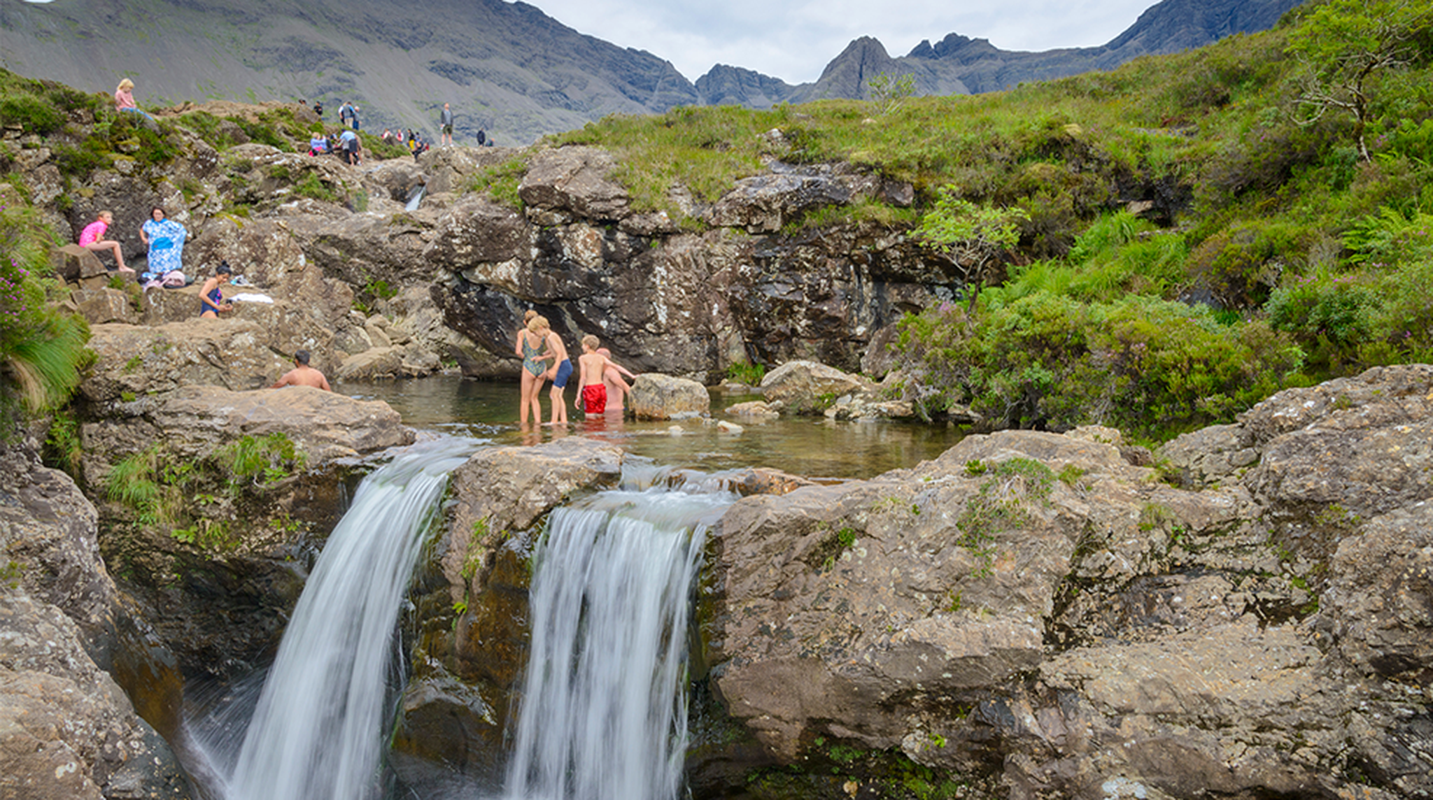 People swimming and paddling in the waters of the Fairy Pools and falls.