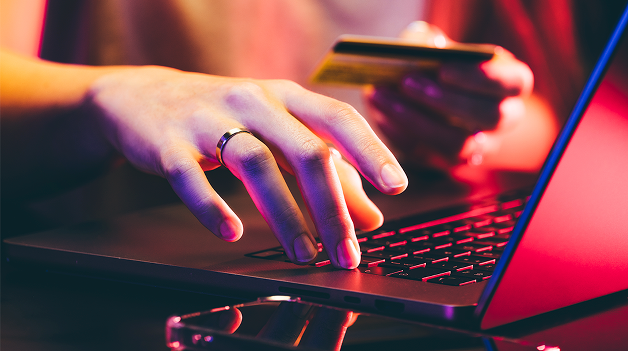 Hands typing on a laptop keyboard, one holding a credit card