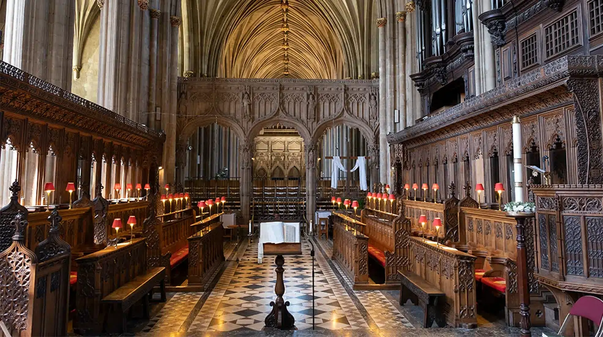 Gothic cathedral interior with ornate wooden pews, vaulted ceilings, and a checkered floor