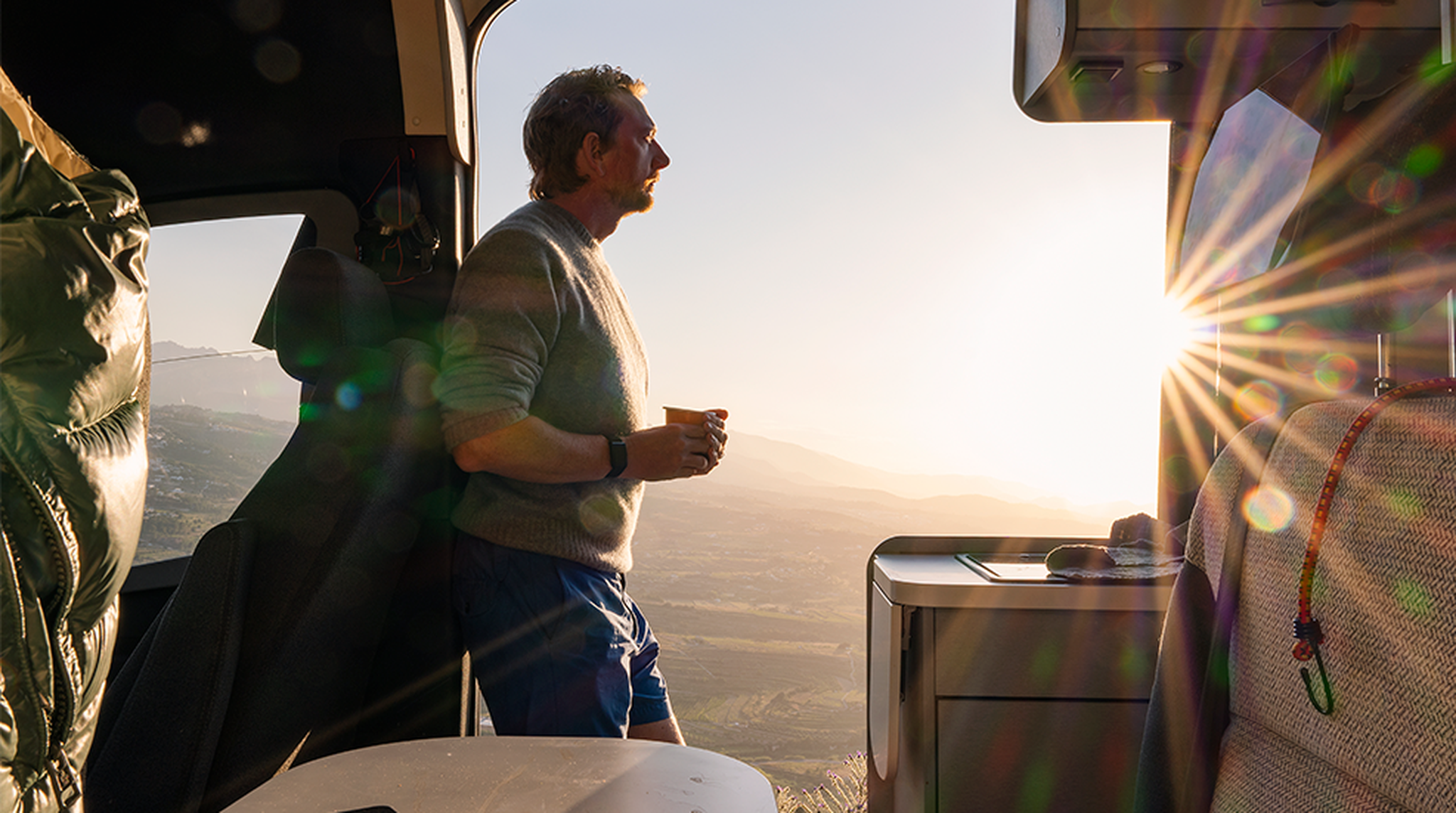 A mature man takes in the sunset view from his campervan parked up in the Spanish mountains