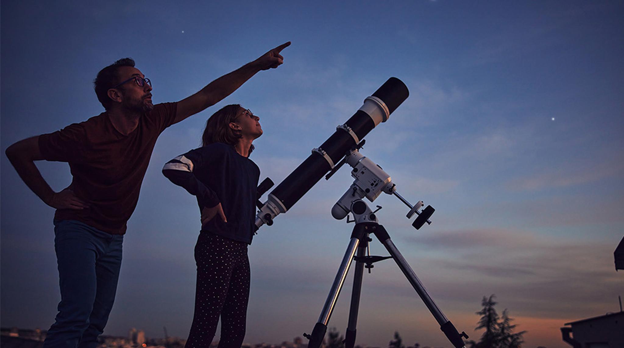 Two people observe the night sky with a telescope