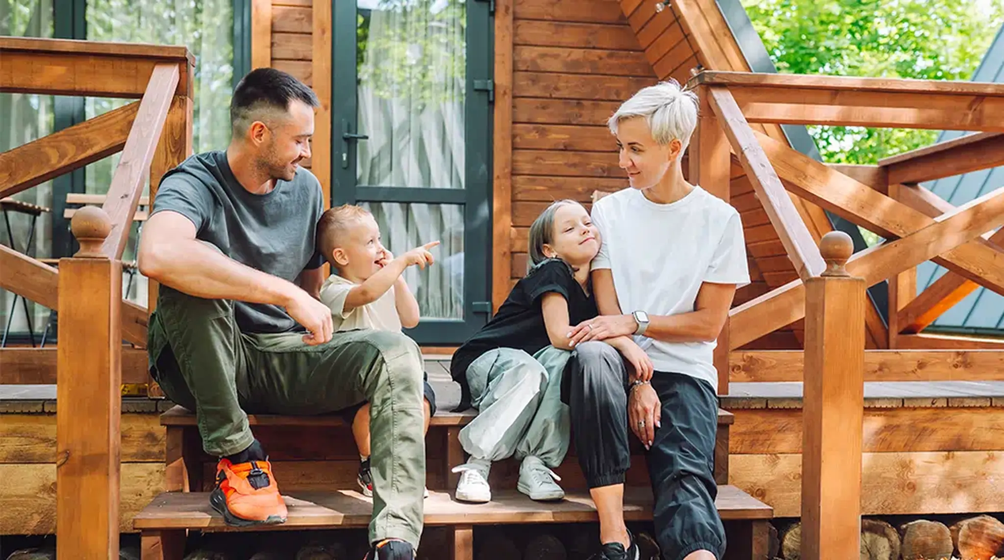 A family of four sitting on wooden steps outside a cabin