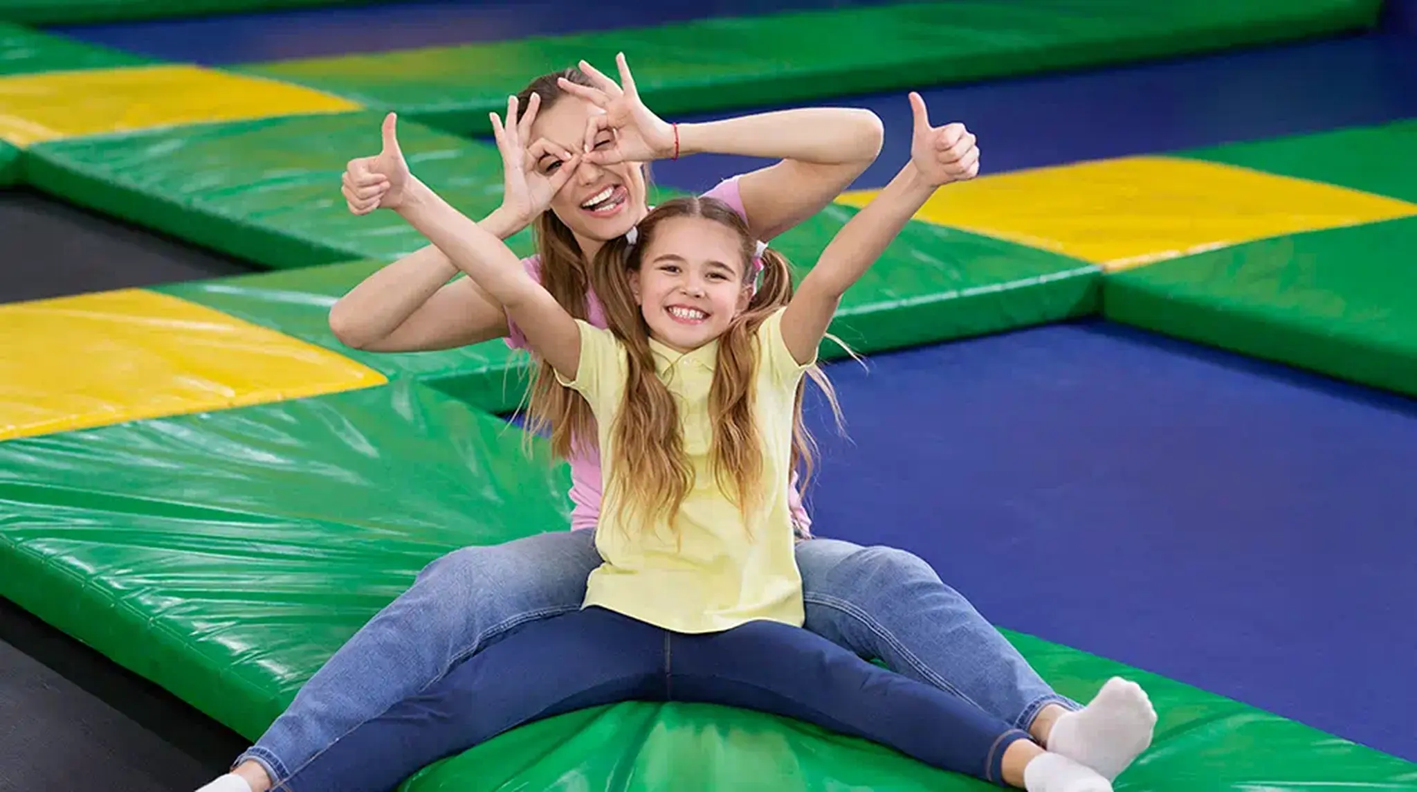 Woman and girl sitting on colourful mats, giving thumbs up and making a playful gesture