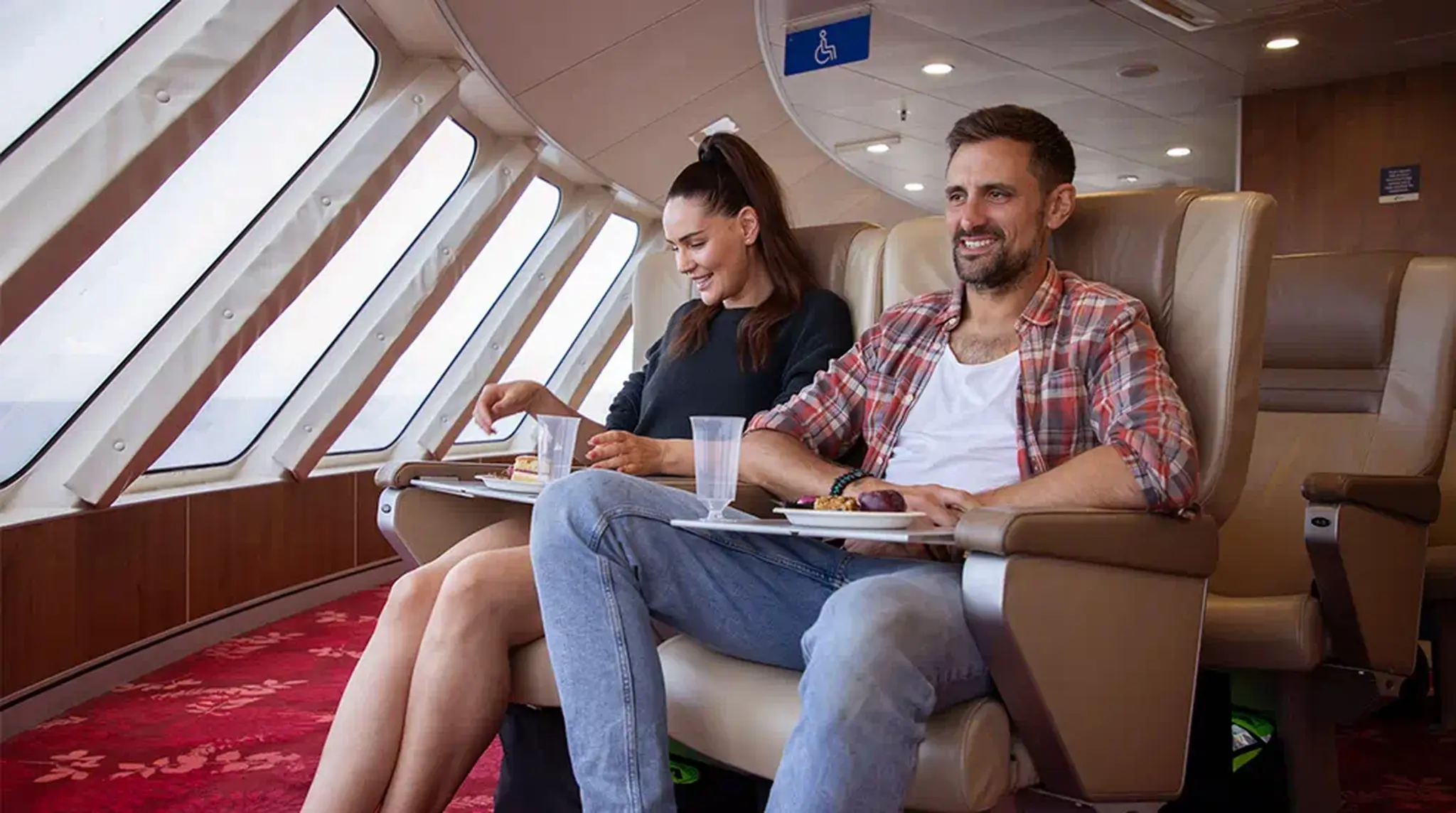 A woman and man relax in comfortable seats on a ferry, enjoying snacks on trays