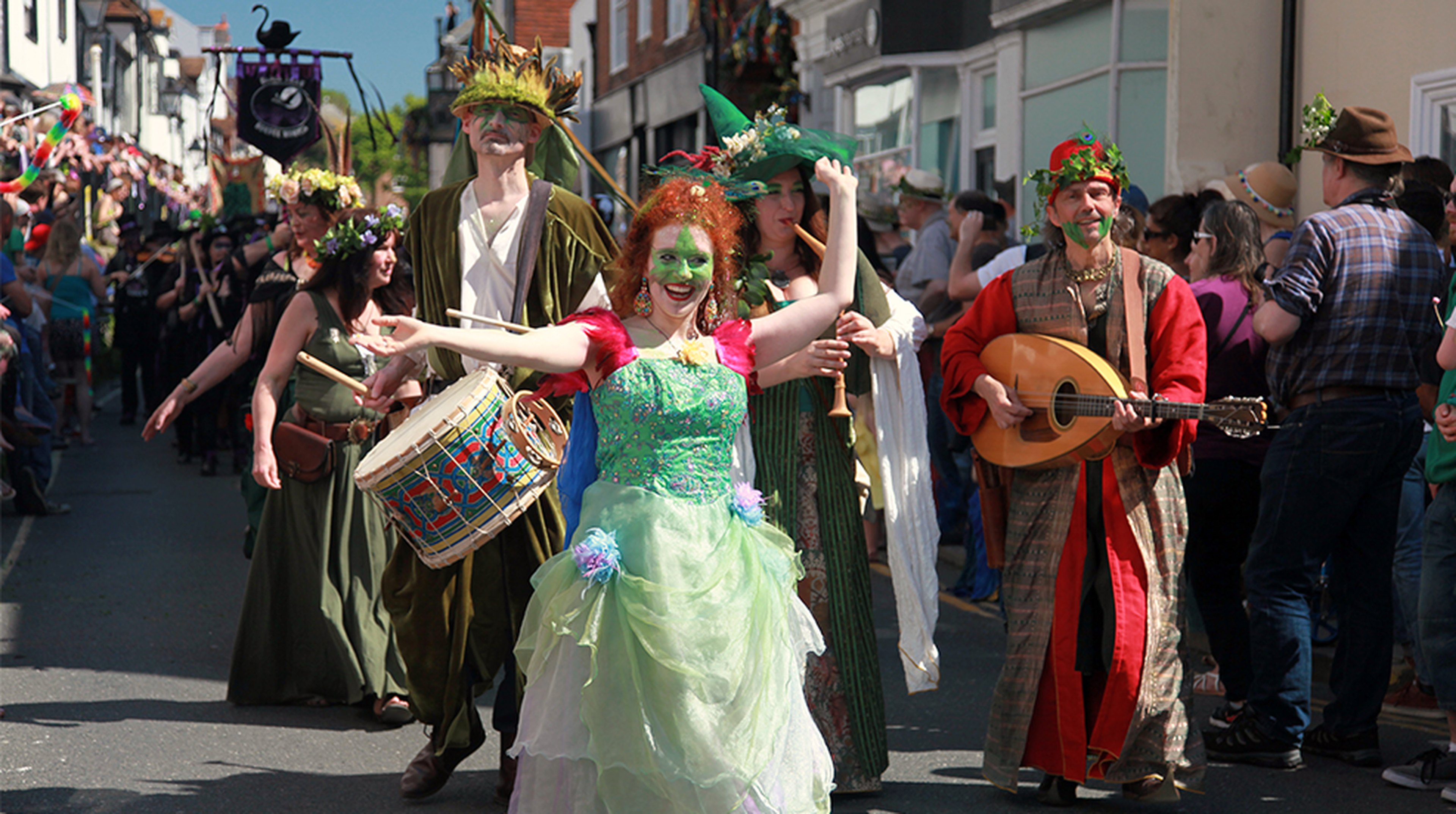 Participants in vibrant costumes parade through a crowded street during a lively outdoor festival.