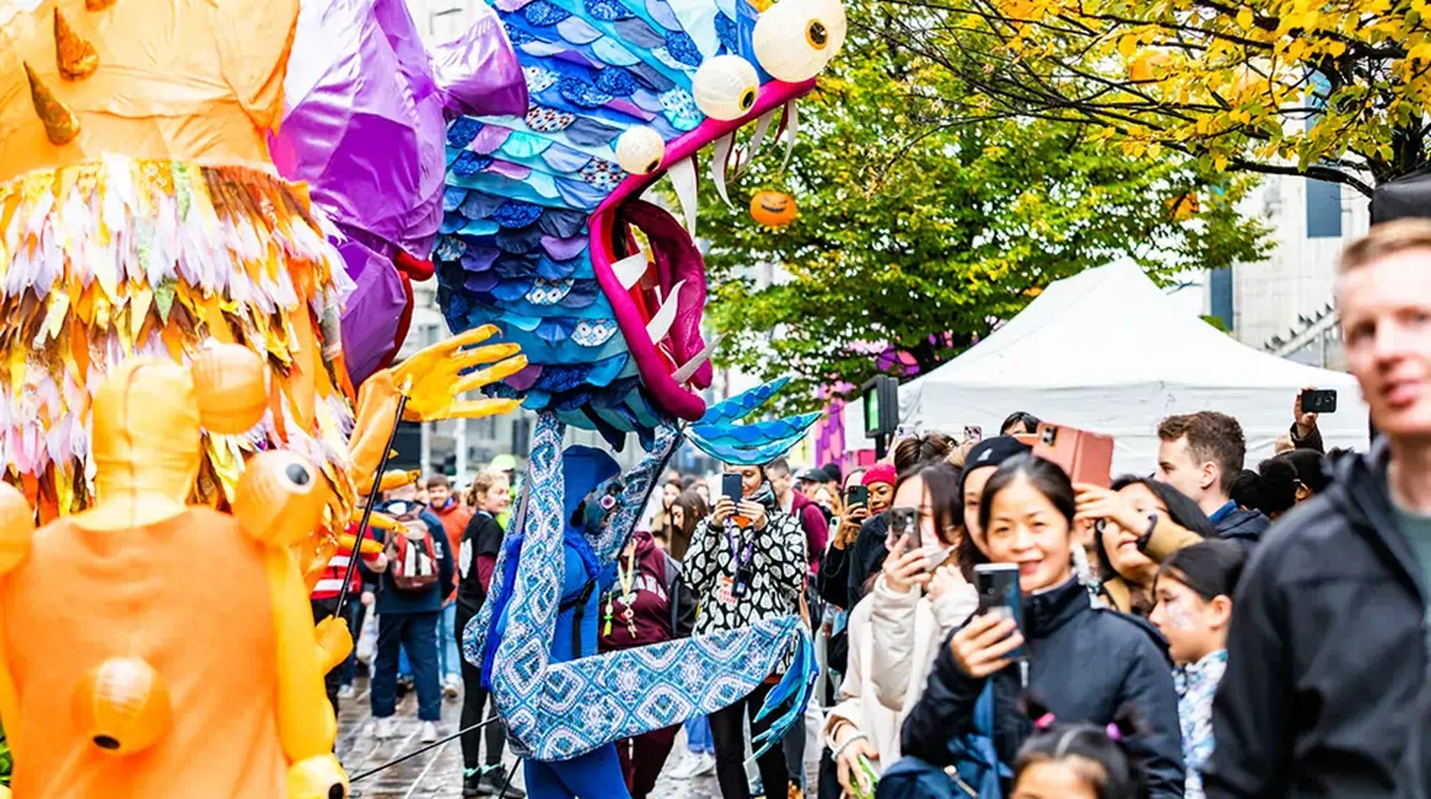 Vibrant street parade with colourful, large puppet costumes and a crowd of people observing and taking photos