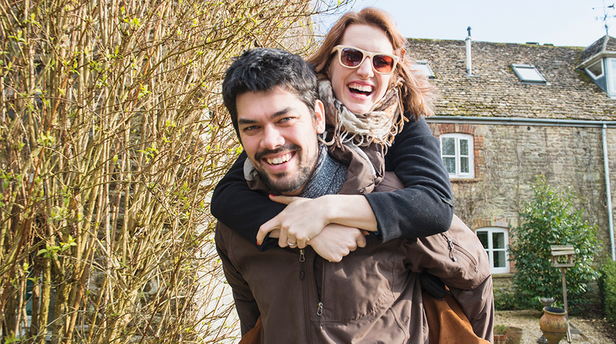 A woman wearing sunglasses playfully rides piggyback on a man
