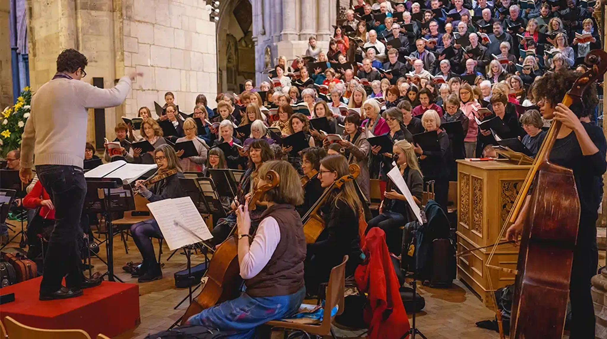 Orchestra and large choir performing in a cathedral, with a conductor leading