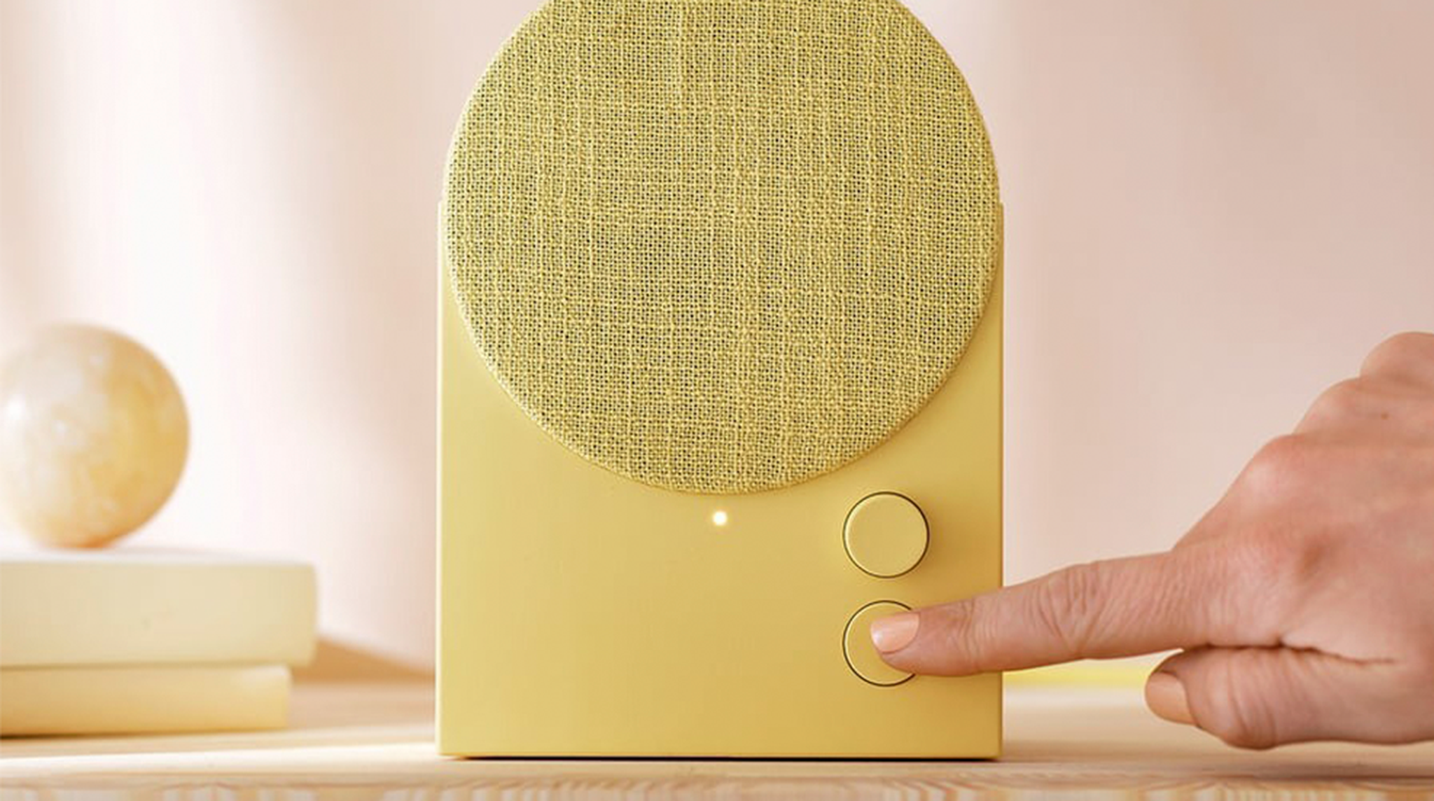 A person presses a button on a yellow, IKEA Nattbad Bluetooth speaker
