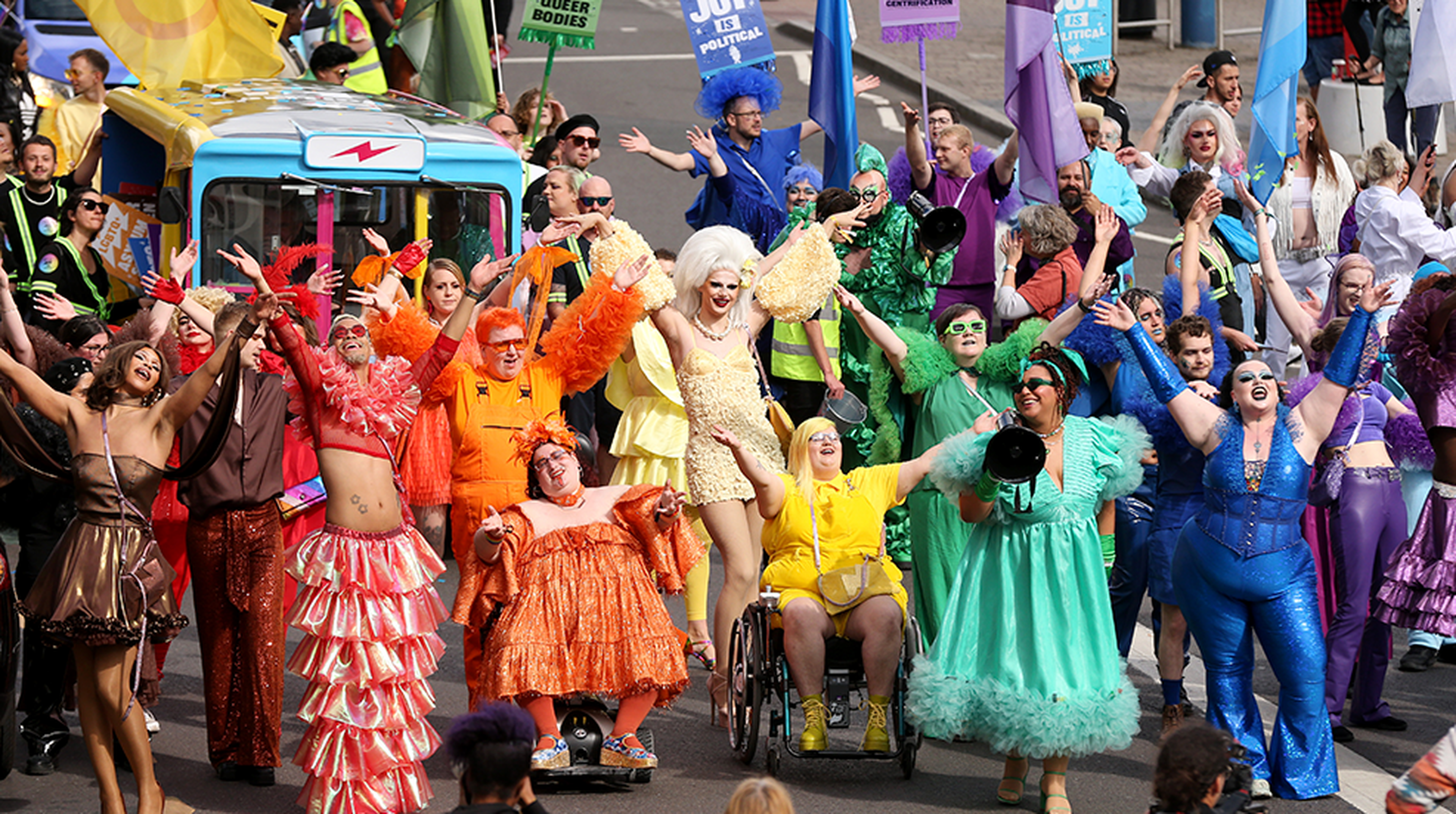 Vibrant parade with participants in colorful outfits, including one in a wheelchair, celebrating diversity and expression on a city street.