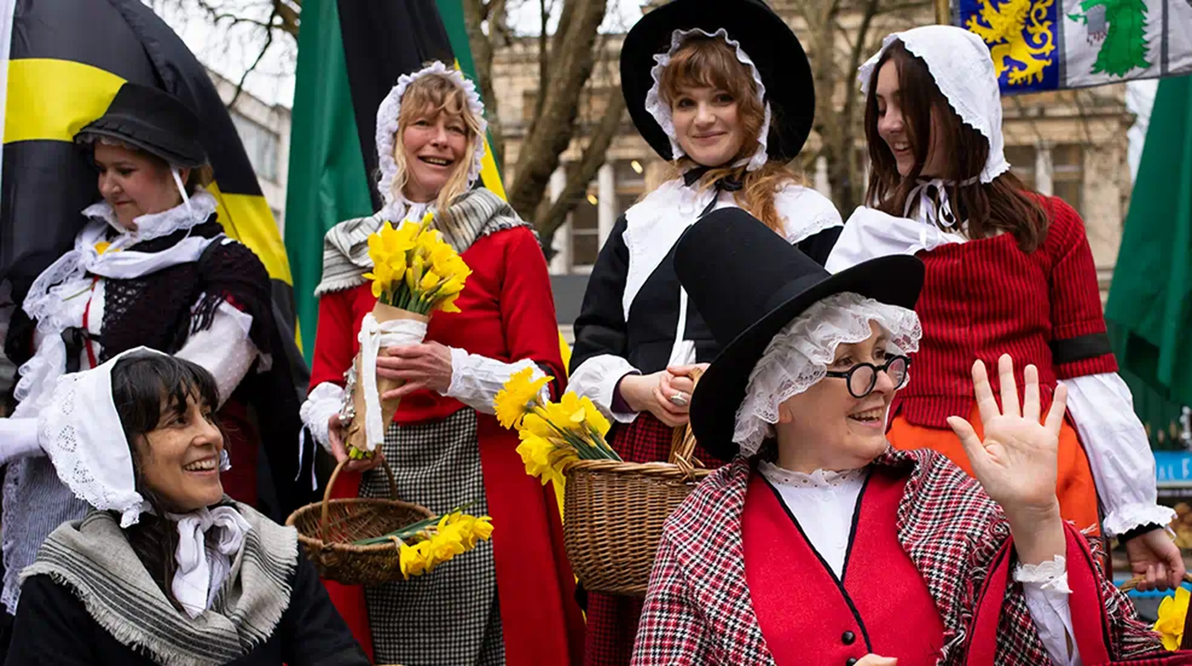 A group of people in traditional Welsh costumes hold daffodils and smile during a celebration outdoors