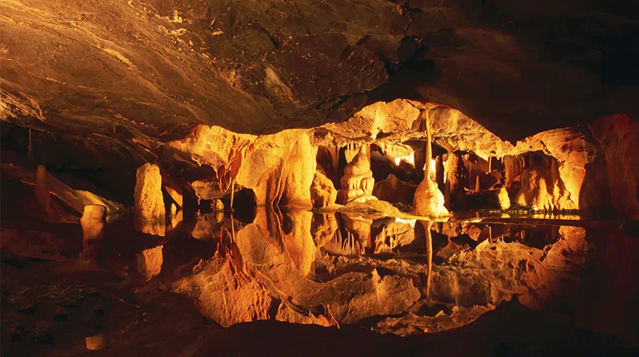 Illuminated cave interior with stalactites and stalagmites reflecting in a pool of water