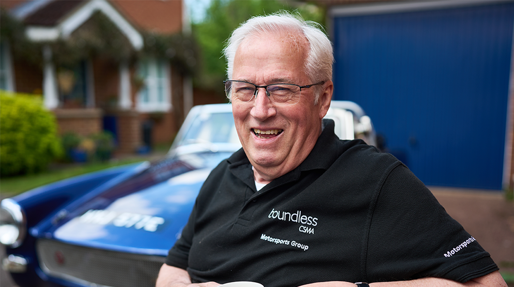 Mike Harrison in the foreground smiling with classic car out of focus in the background