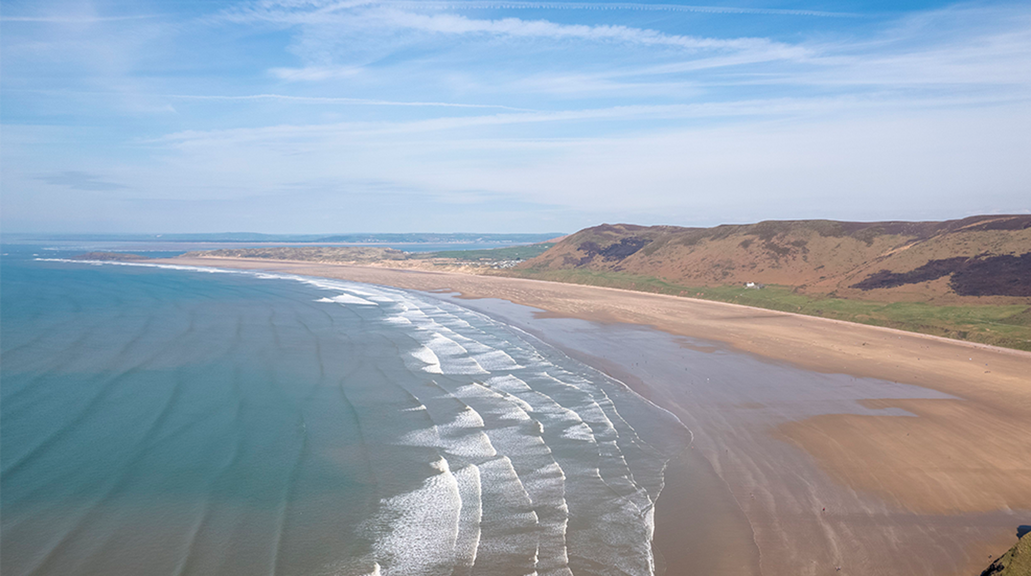An expansive aerial view of Rhossili Bay in Wales, showcasing its pristine beach and sweeping coastline.