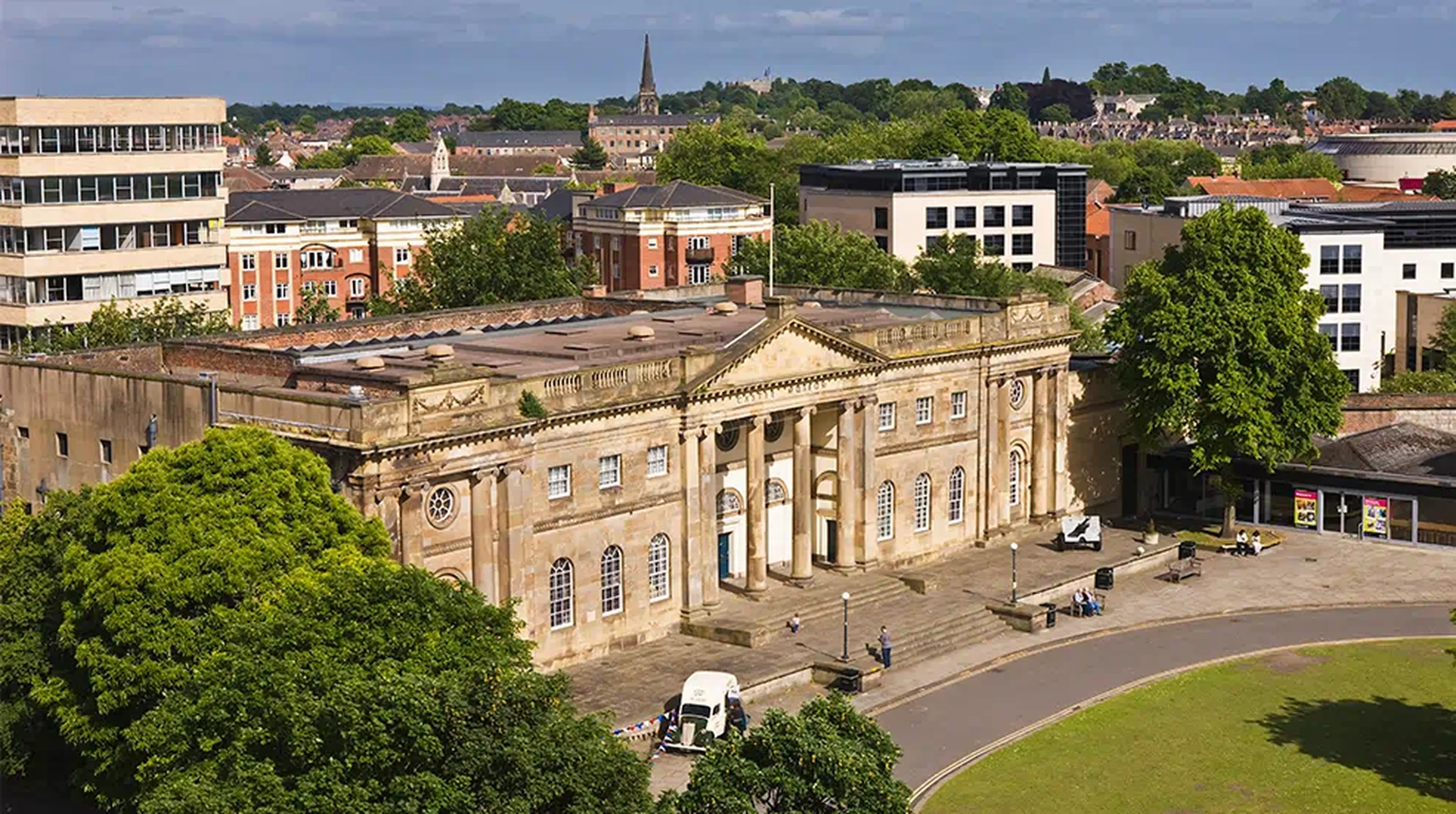 Aerial view of a historic neoclassical stone building with columns, surrounded by greenery