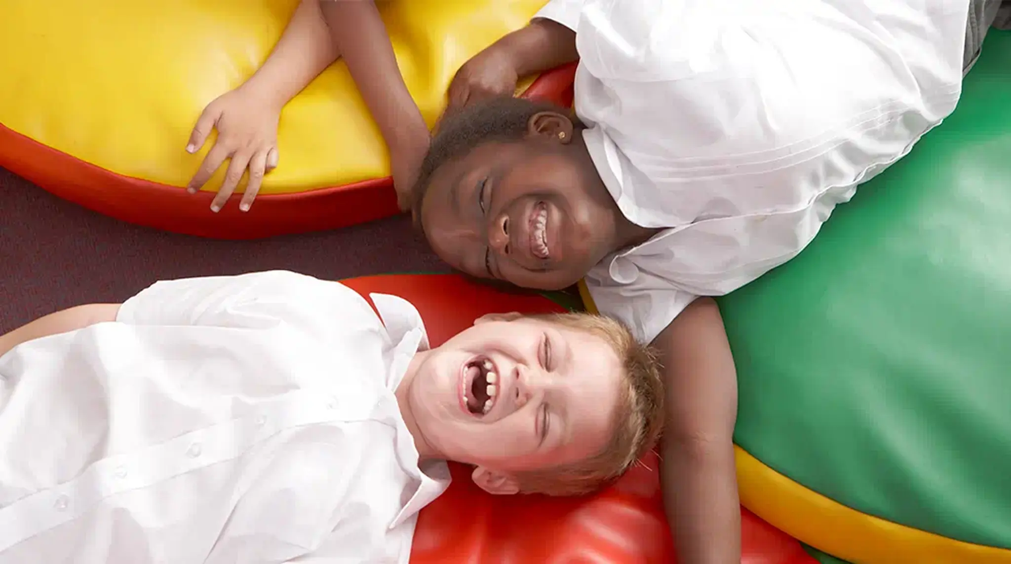 Two children in white shirts lying on colourful bean bags, laughing