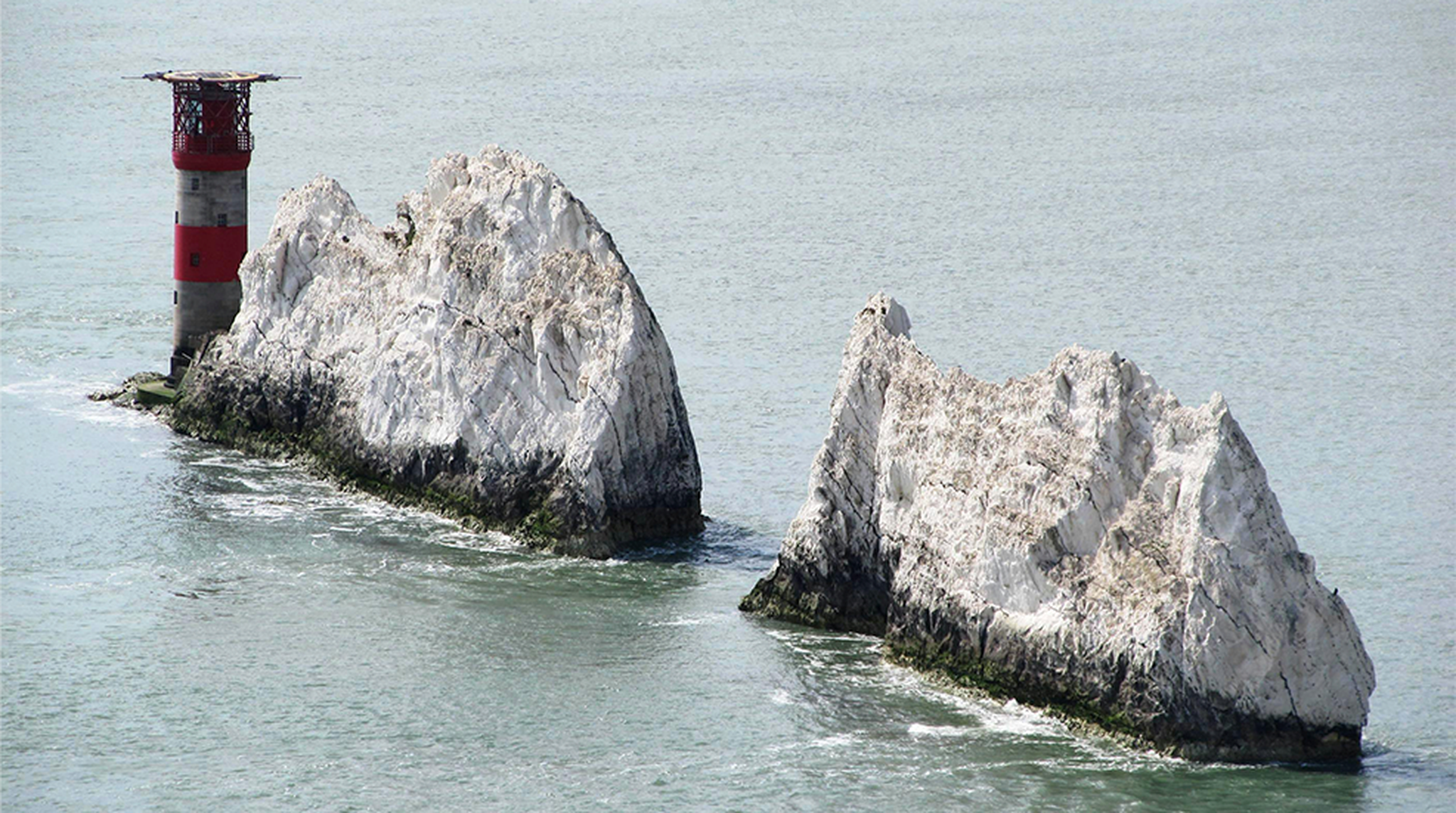 An iconic view of The Needles rock formation and lighthouse on the Isle of Wight, England, under clear skies.