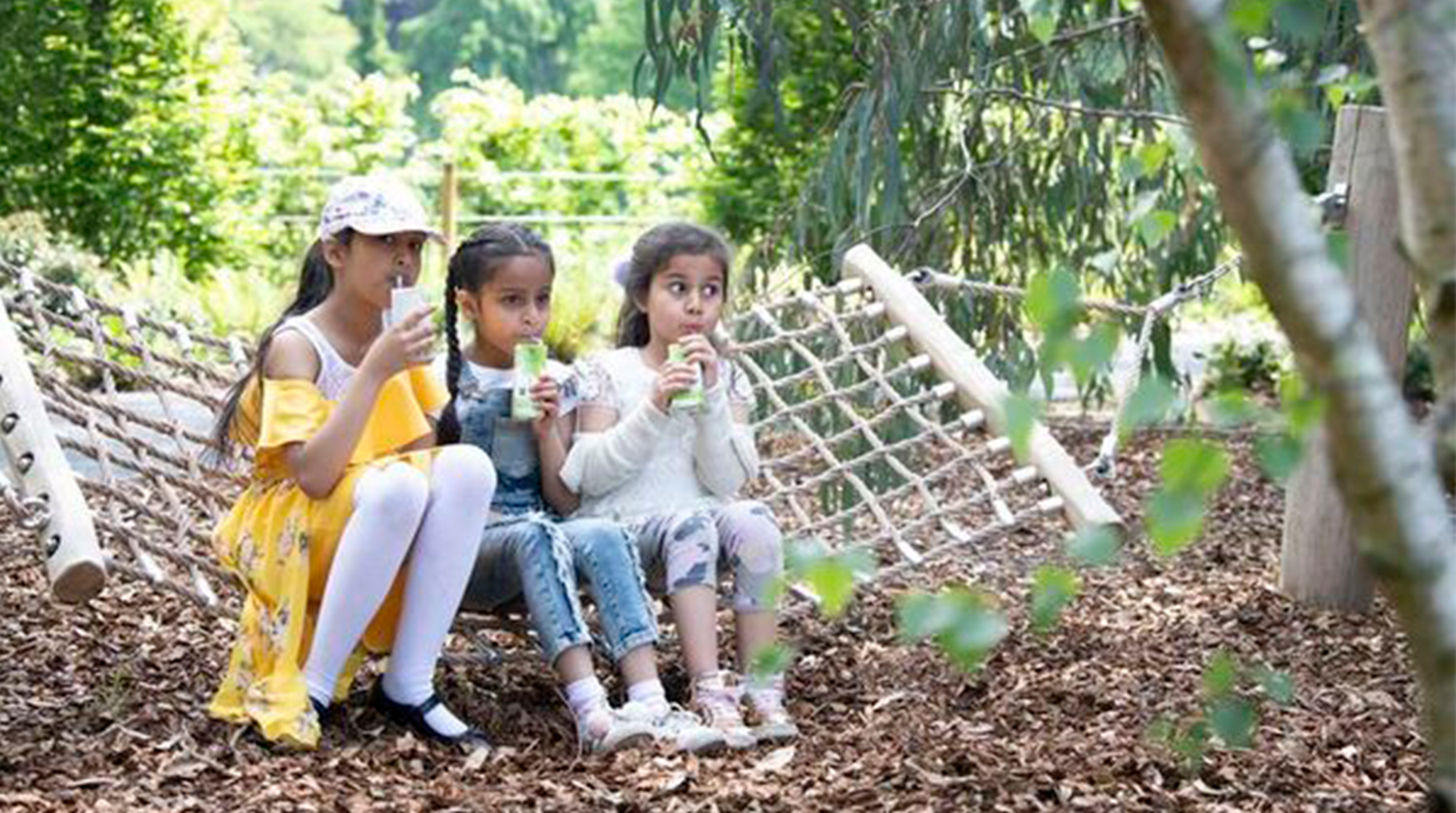 Three girls sat on hammock drinking juice cartons