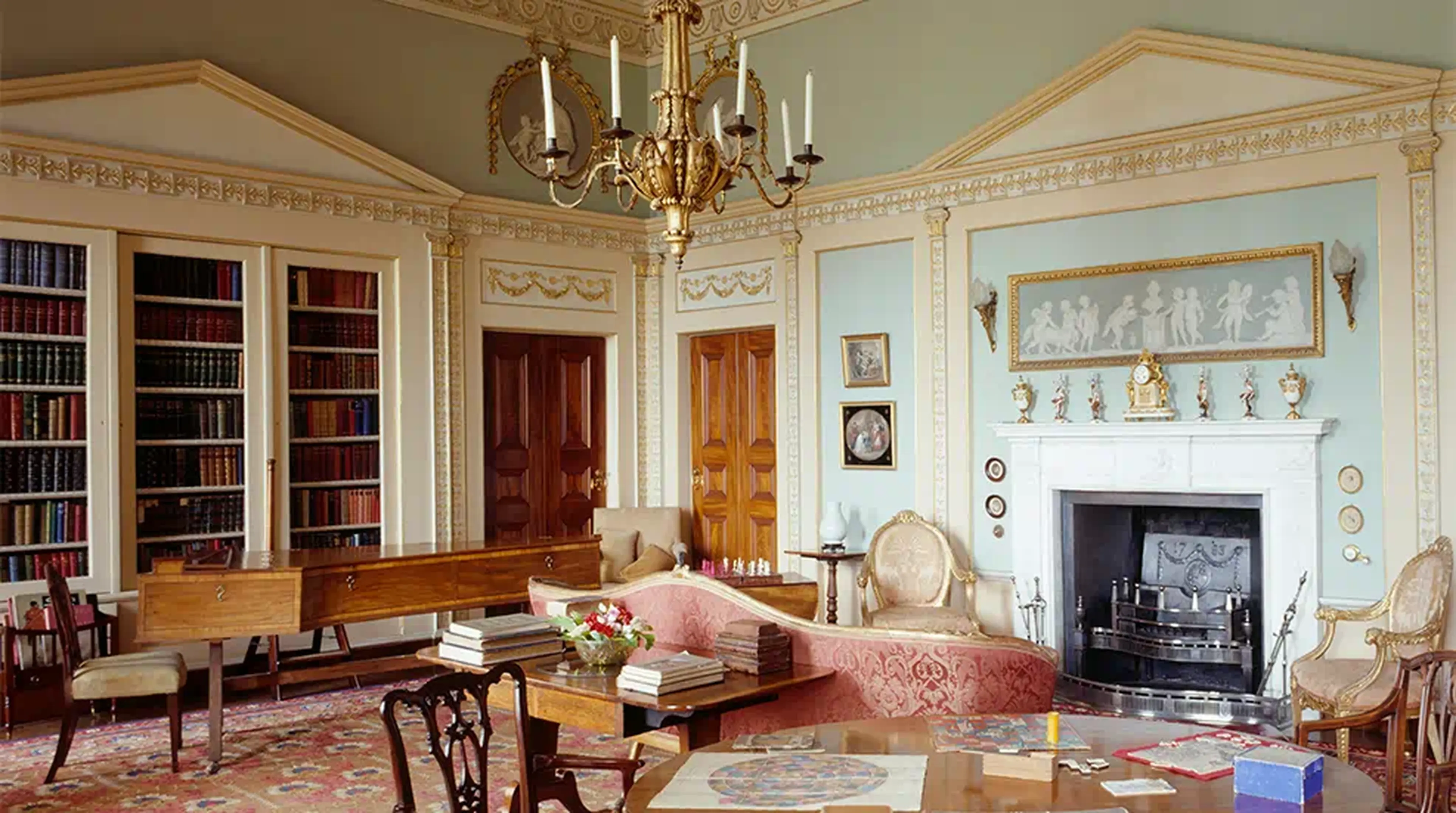 Elegant library with classical decor, ornate chandelier, bookshelves, fireplace, and antique furniture