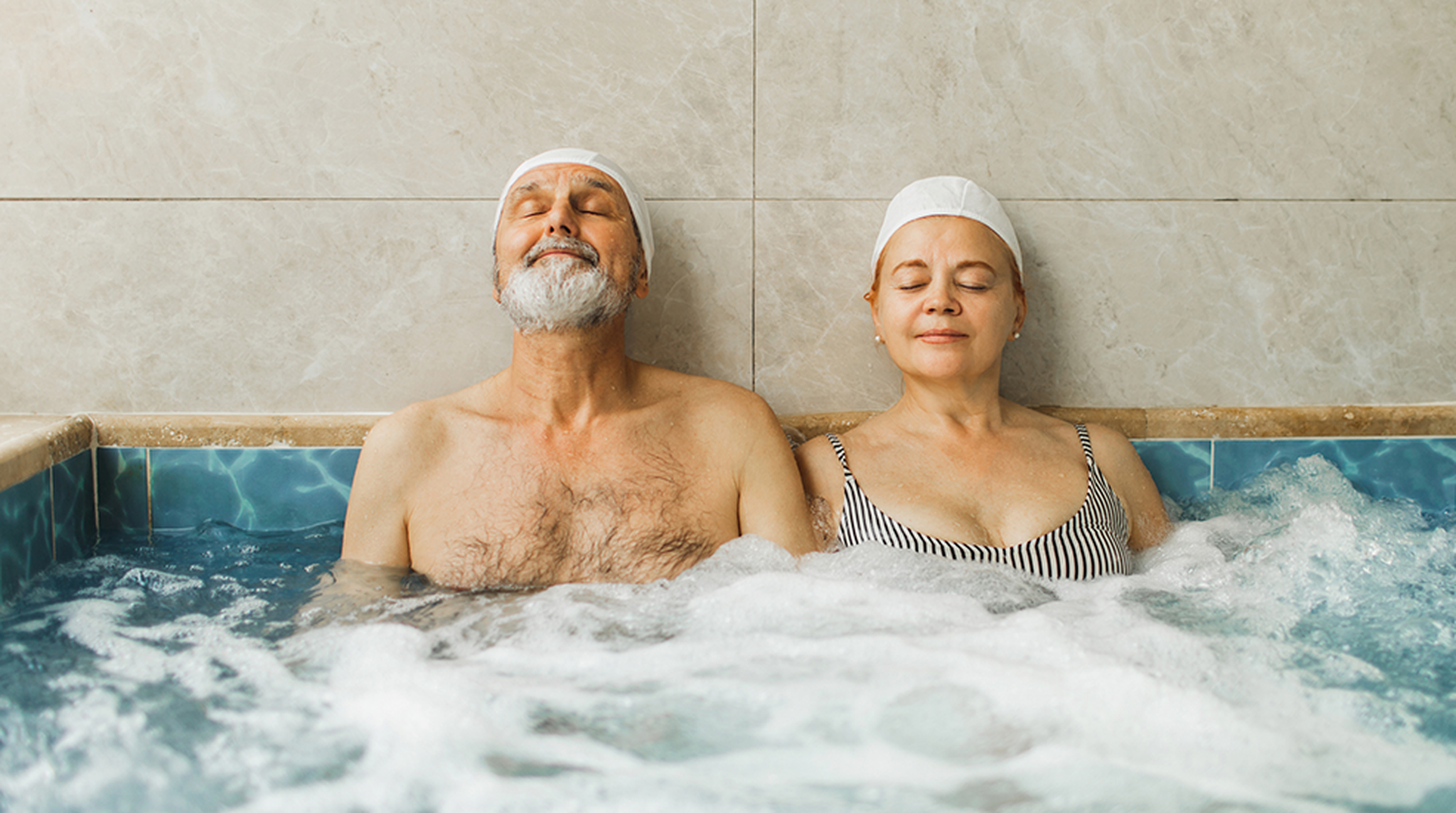 A senior couple sat side by side in a hot tub looking content and relaxed