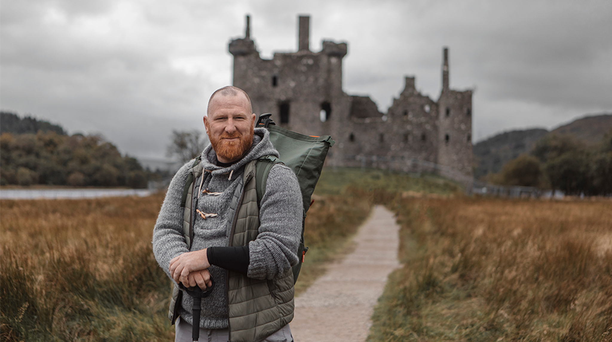 Man with a red beard stands on a path in front of a historic stone castle