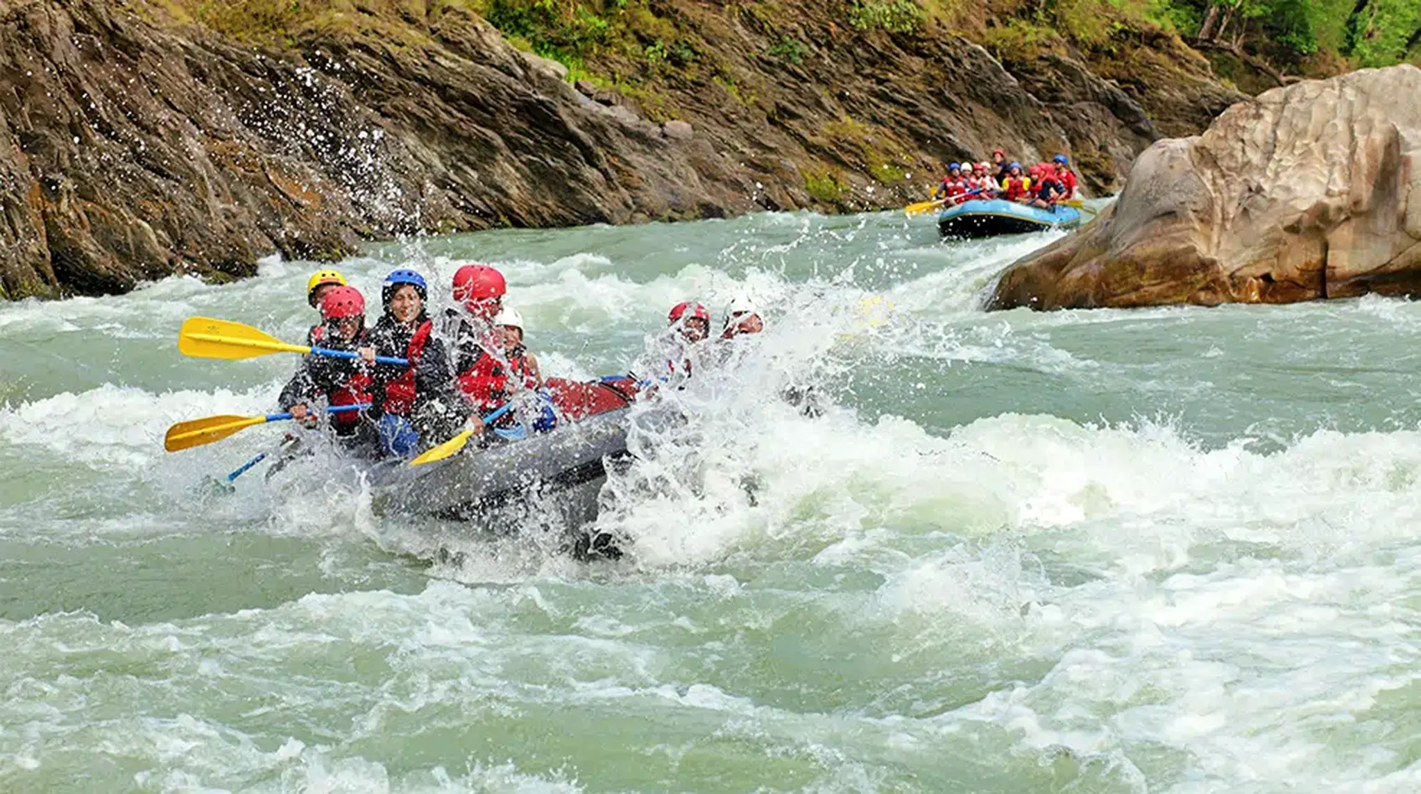 A group of people in helmets and life jackets white-water rafting down a river