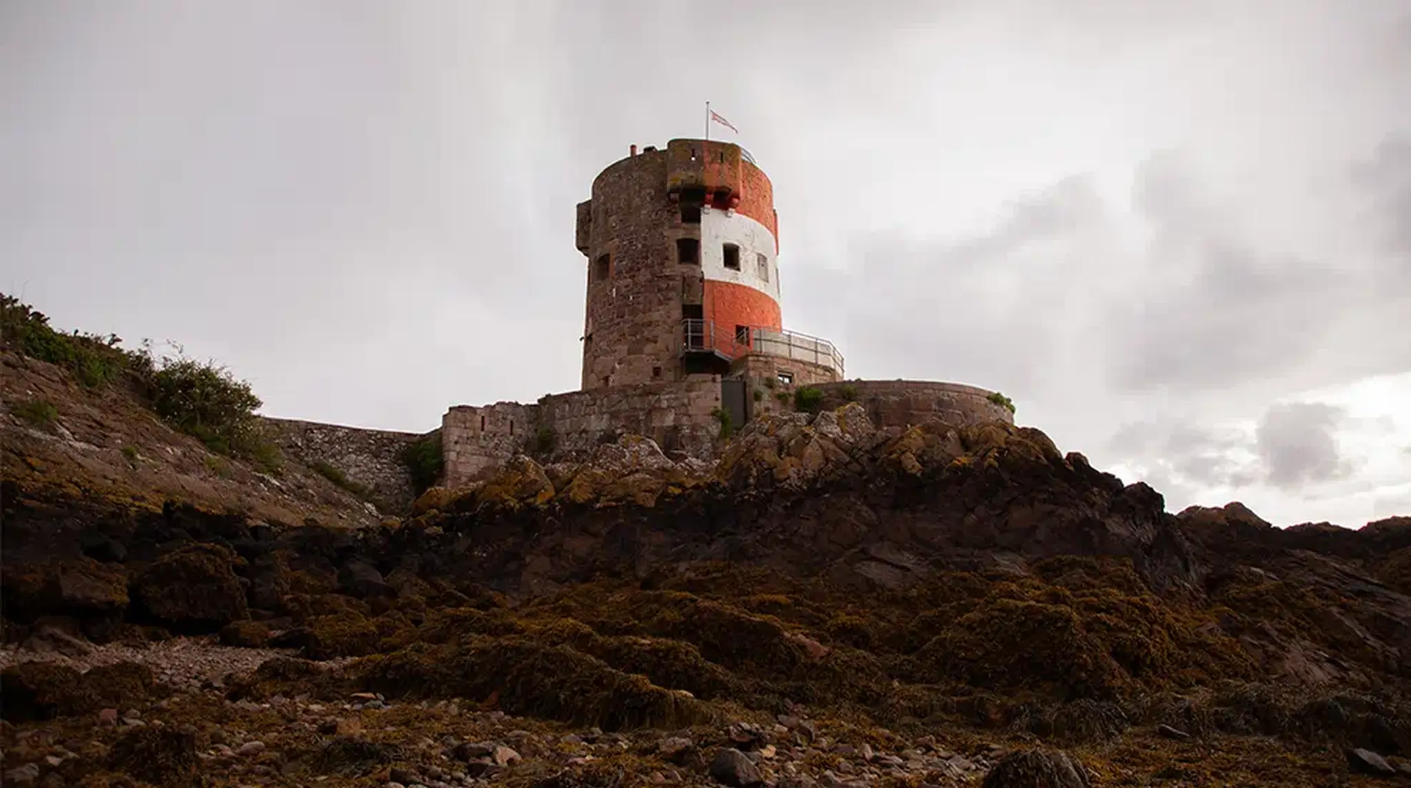 Historic stone tower with red and white stripes, atop rocky terrain