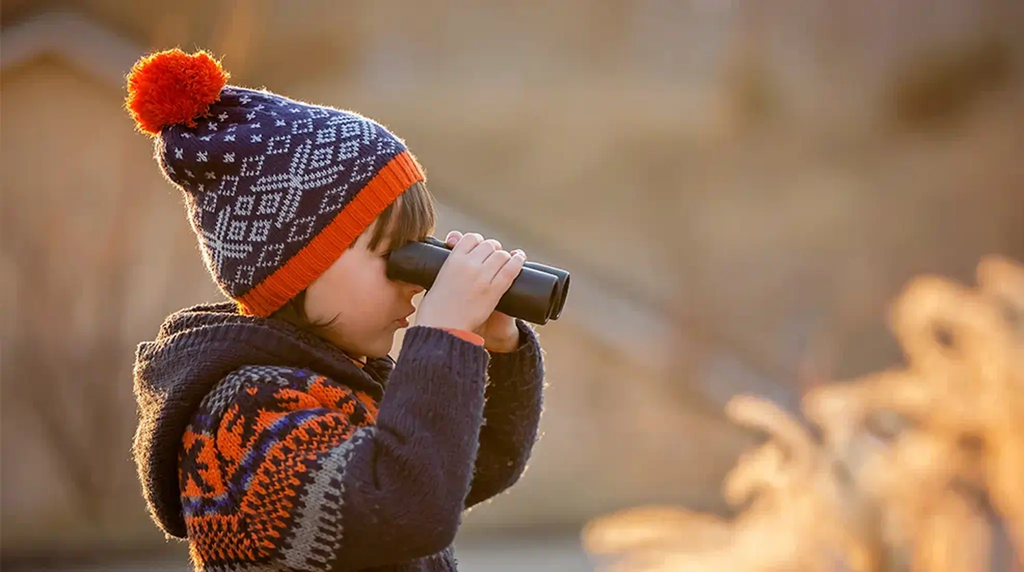 A child in winter hat and sweater uses binoculars outdoors