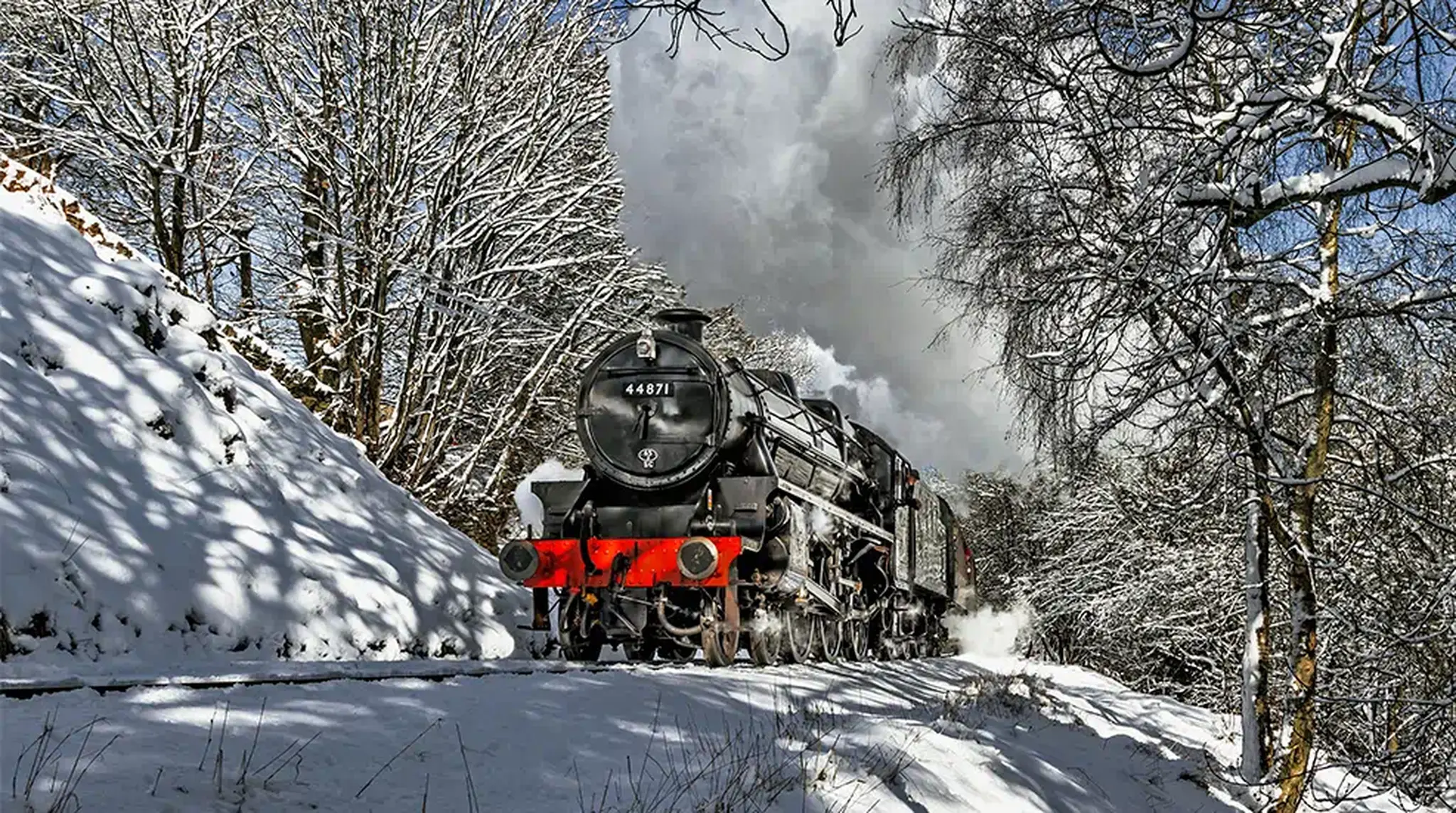 Steam train travelling through a snowy landscape, surrounded by snow-covered trees