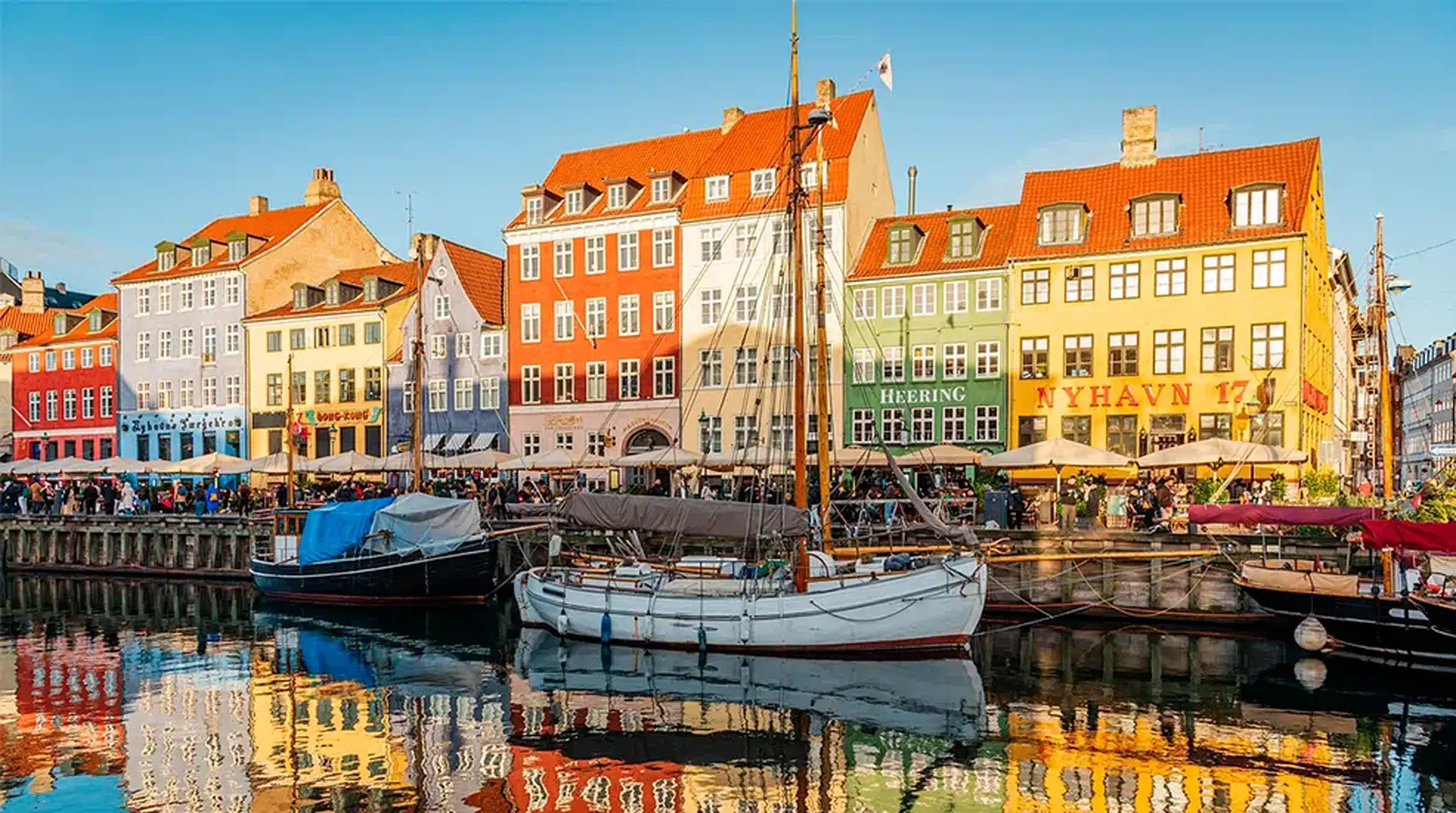 Colourful historic buildings and boats along the Nyhavn canal in Copenhagen, Denmark, under a clear blue sky during sunset.