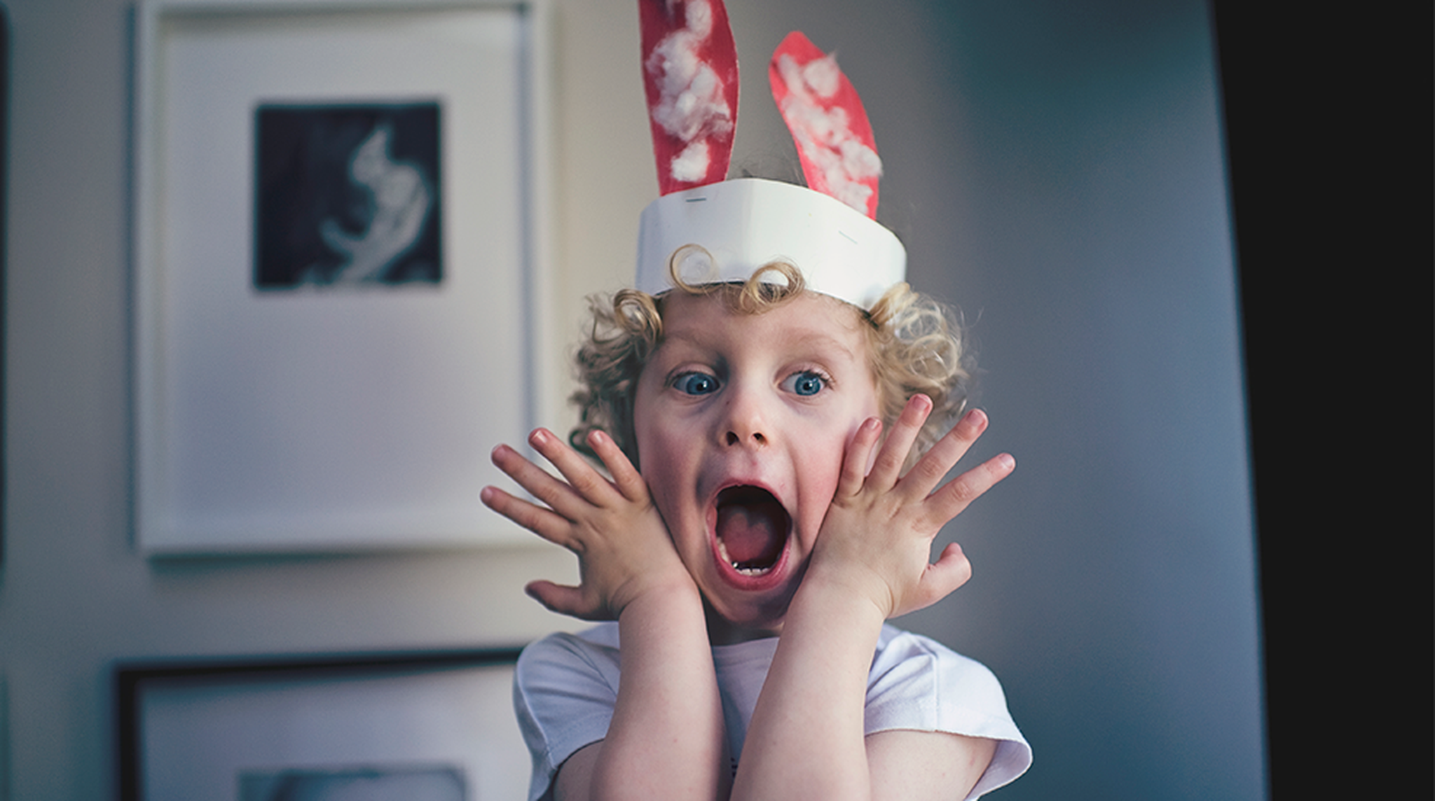 A child with curly hair, wearing a handmade bunny ear hat