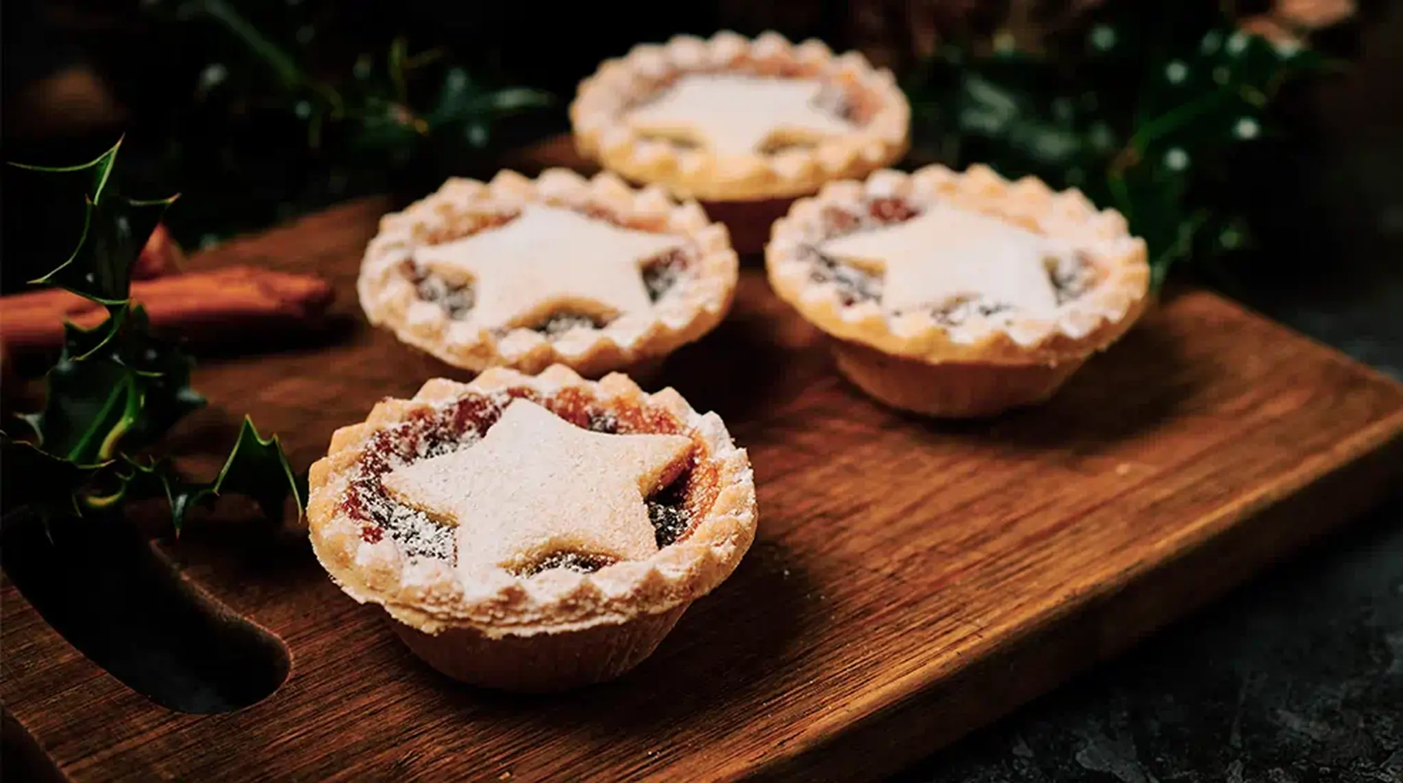 Four star-shaped mince pies dusted with powdered sugar on a wooden board