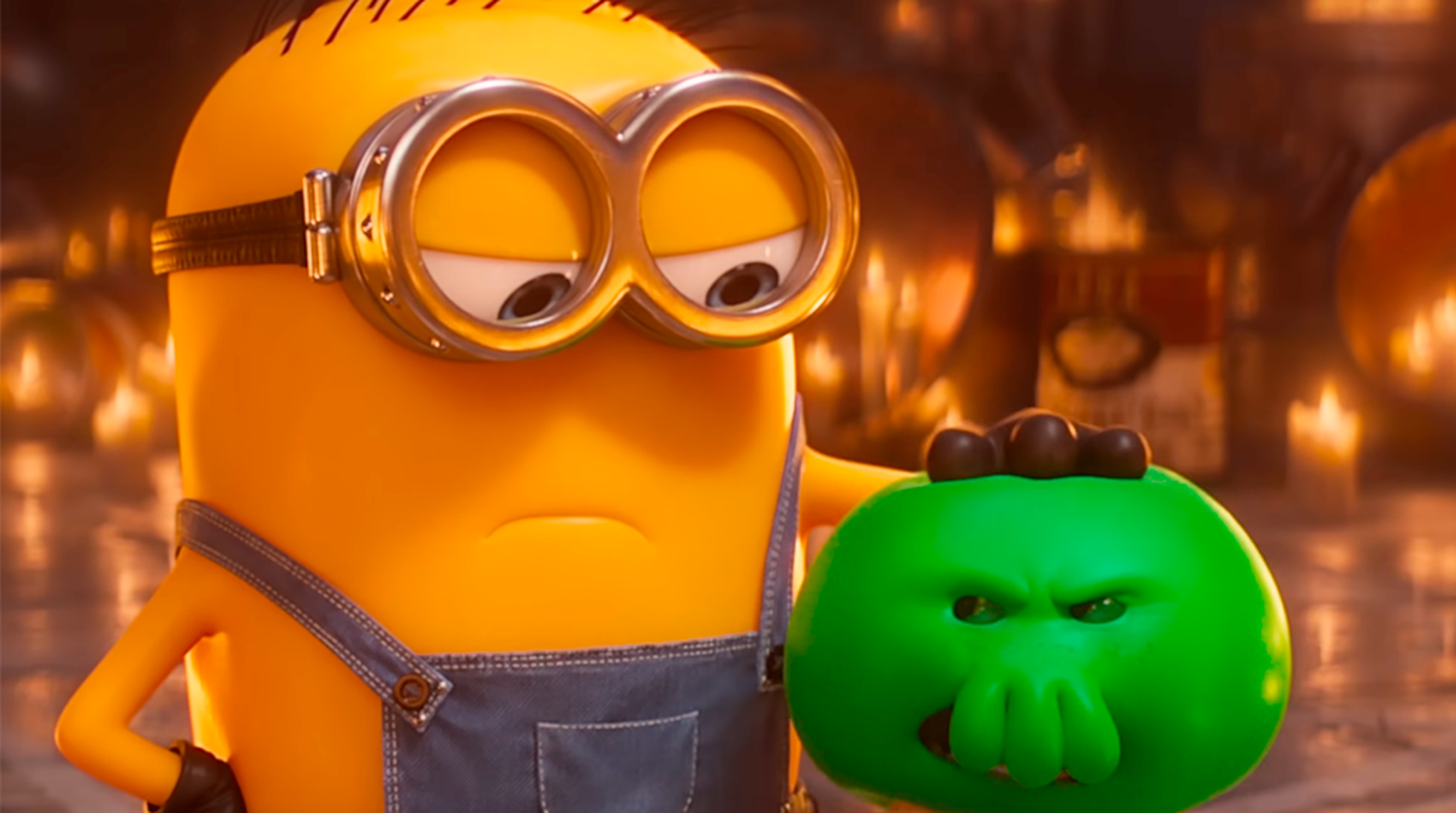 A Minion in overalls holds a green, angry-looking creature in a dimly lit room.