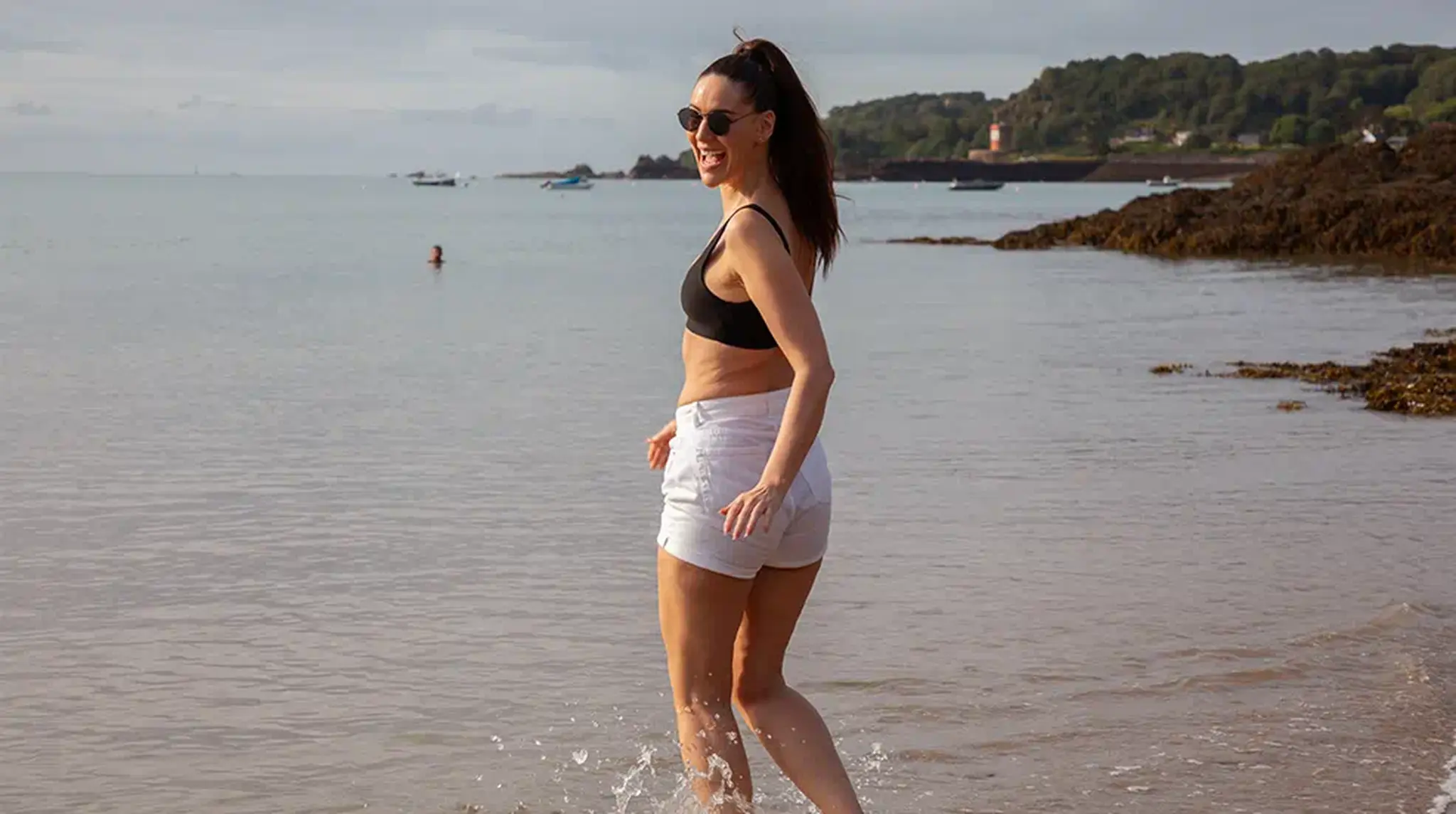 Woman in sunglasses and activewear joyfully wading in the shallow sea