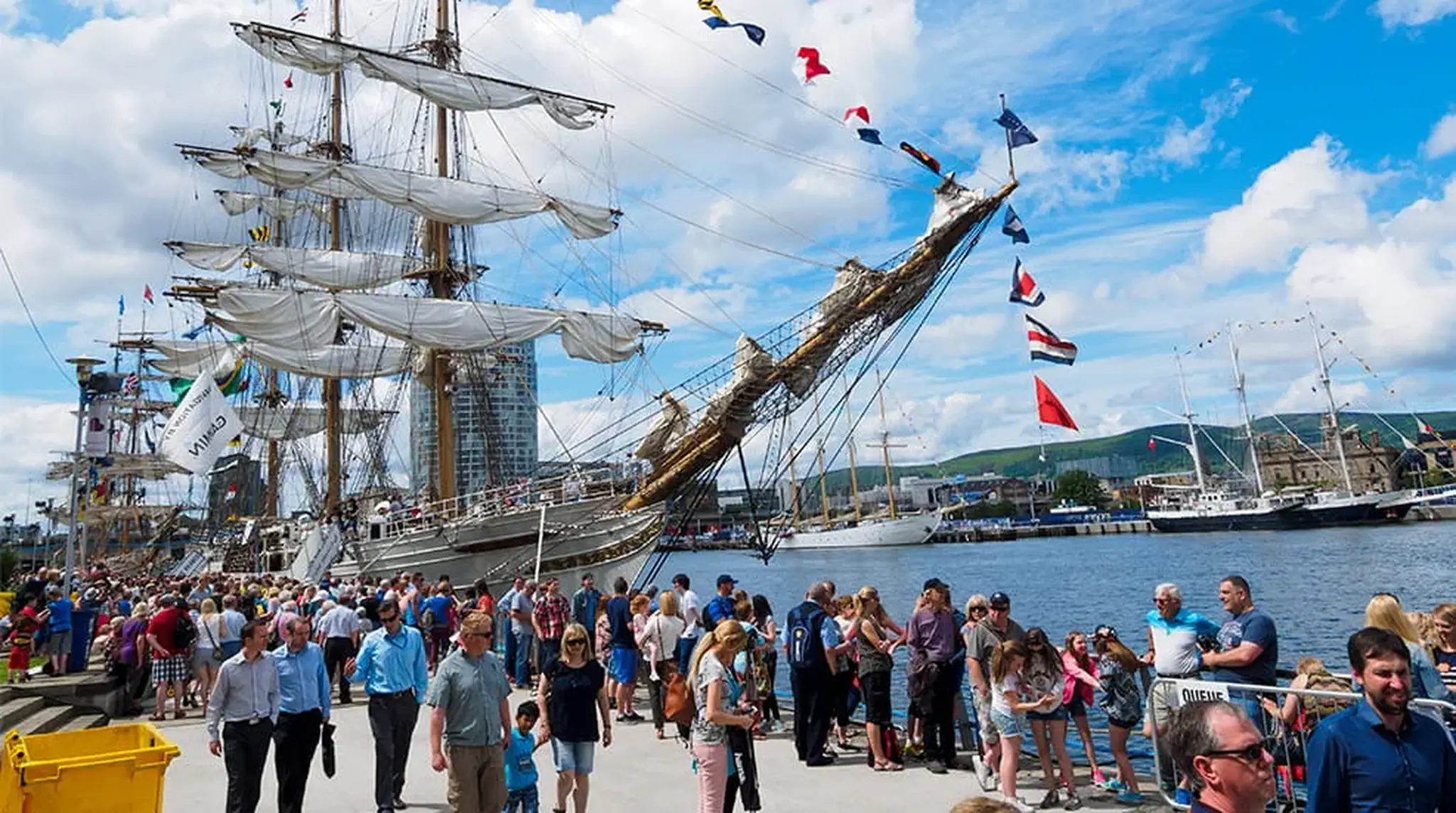 Crowd at a waterfront festival with tall ships docked