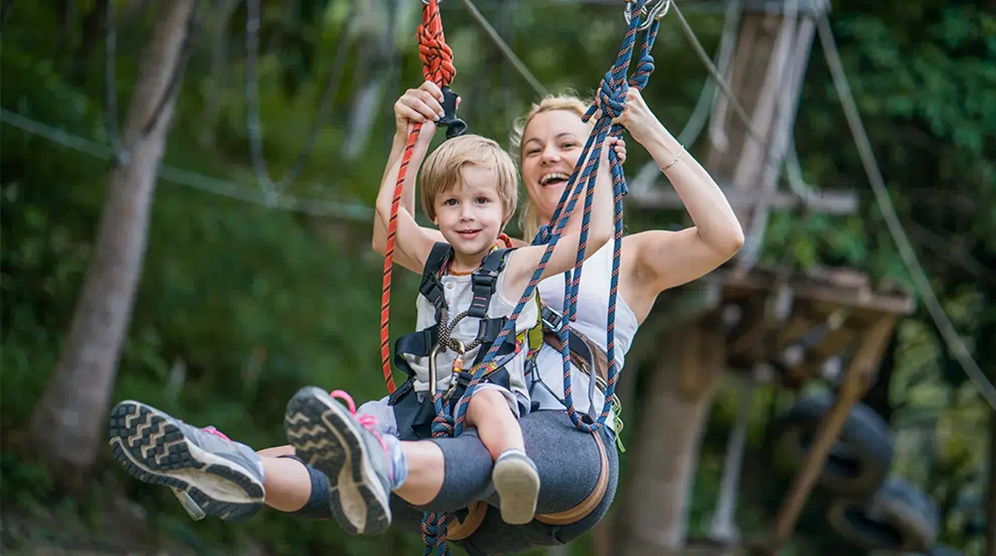 A joyful woman and child wearing harnesses ride a zip line