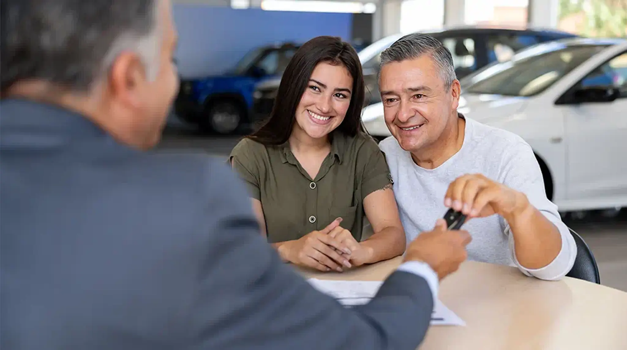 A couple smiling as they receive car keys from a salesperson in a dealership