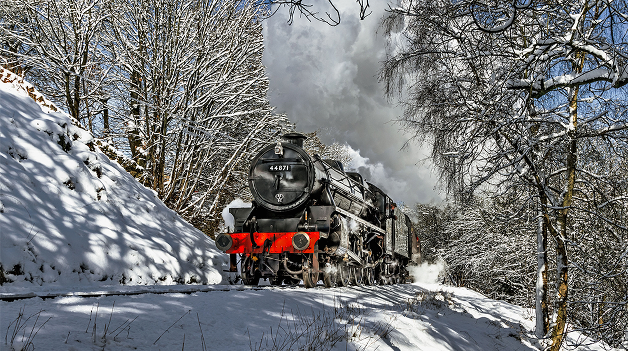 A black steam locomotive travels through a snowy landscape