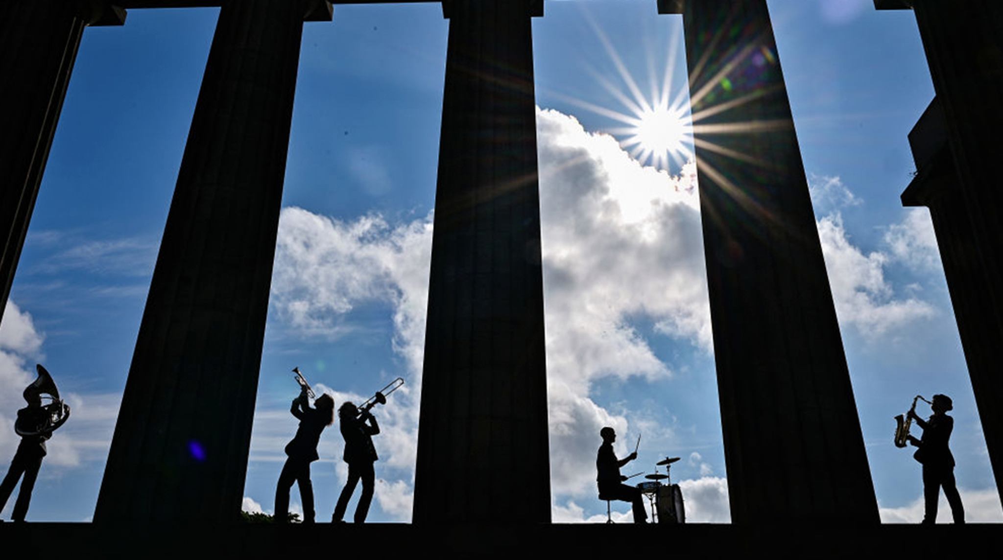 Five members of the band Brass Gumbo play brass instruments in between the columns of the National Monument on Calton Hill, Edinburgh