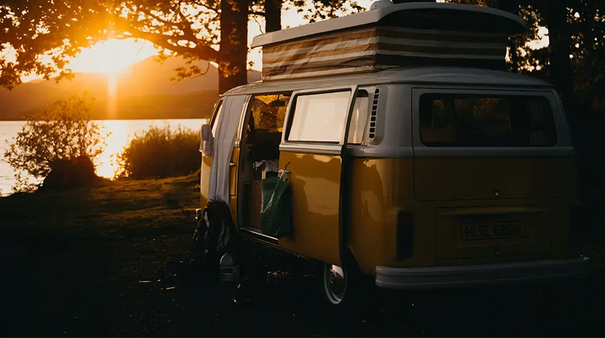 A yellow camper van parked by a lake at sunset