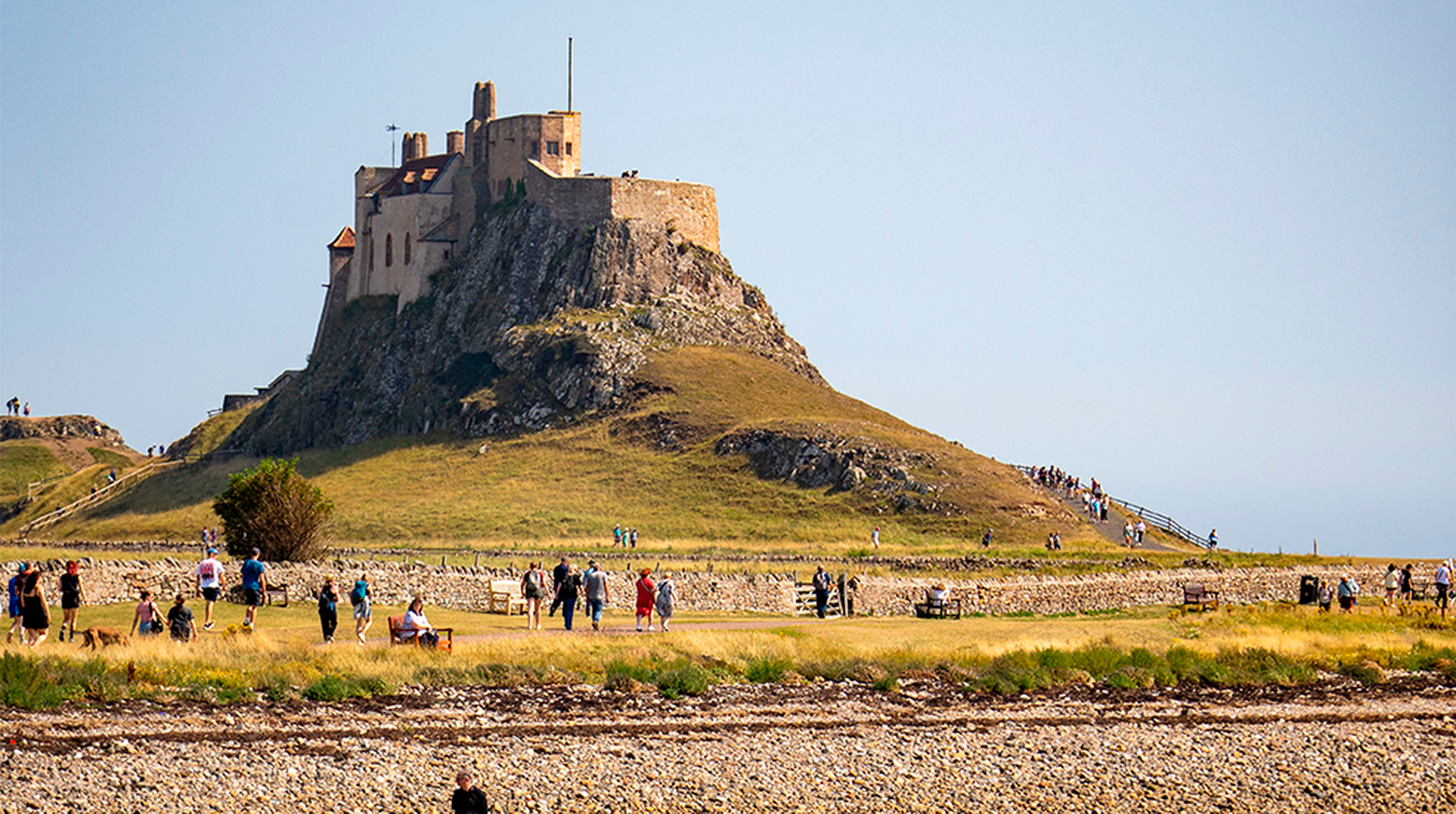 View of Lindisfarne Castle on Holy Island with visitors exploring the rocky shore.