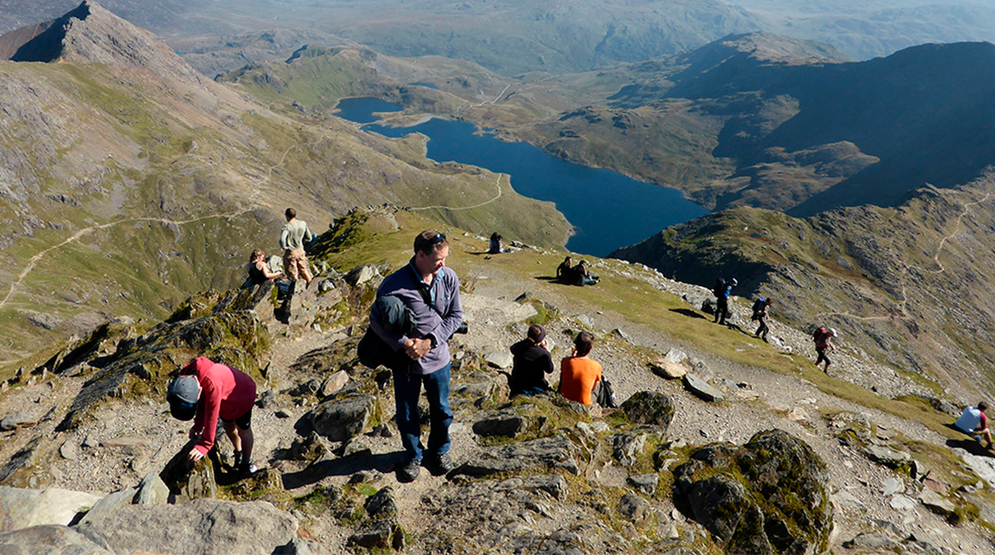 Hikers enjoy a stunning aerial view from the summit of Snowdon, overlooking Llyn Llydaw in North Wales.