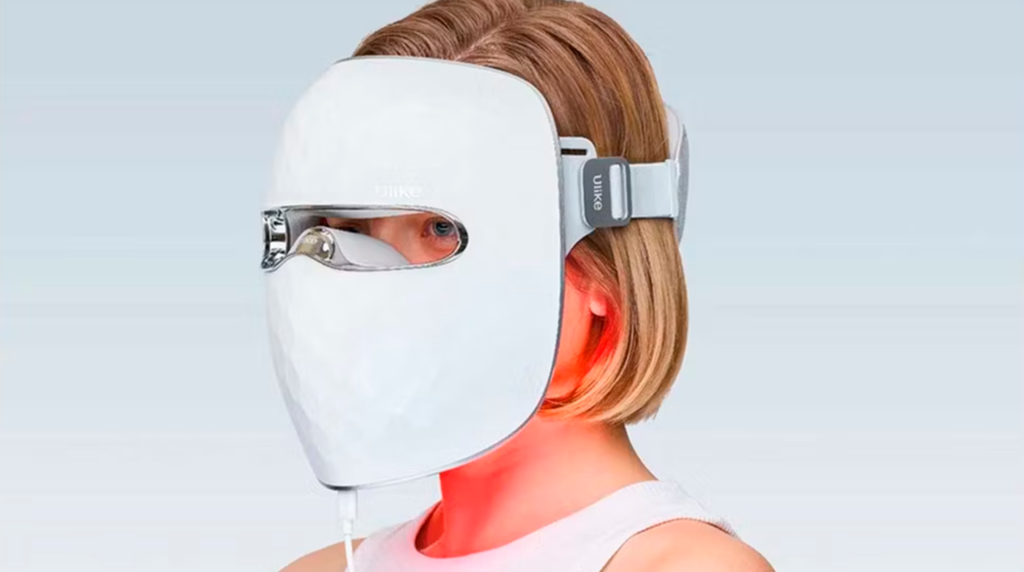 Person wearing a white LED light therapy mask with a strap, emitting a red glow