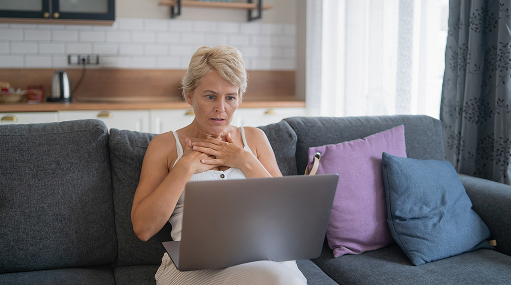 A woman looking surprised while sitting on a couch and using a laptop
