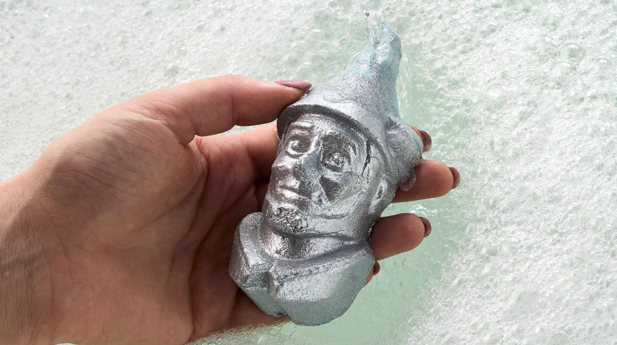 Hand holding a Lush Tin-Man Bubble Bar above bubbly water