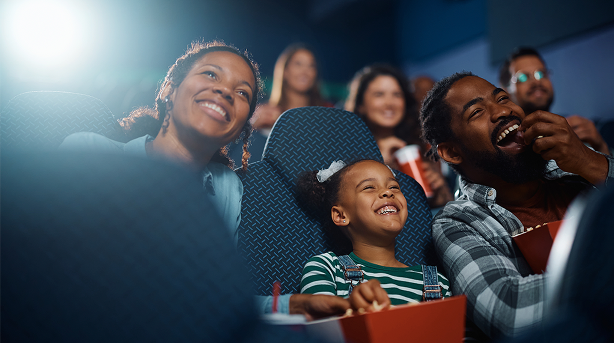 A family of three happily watches a movie in a theater