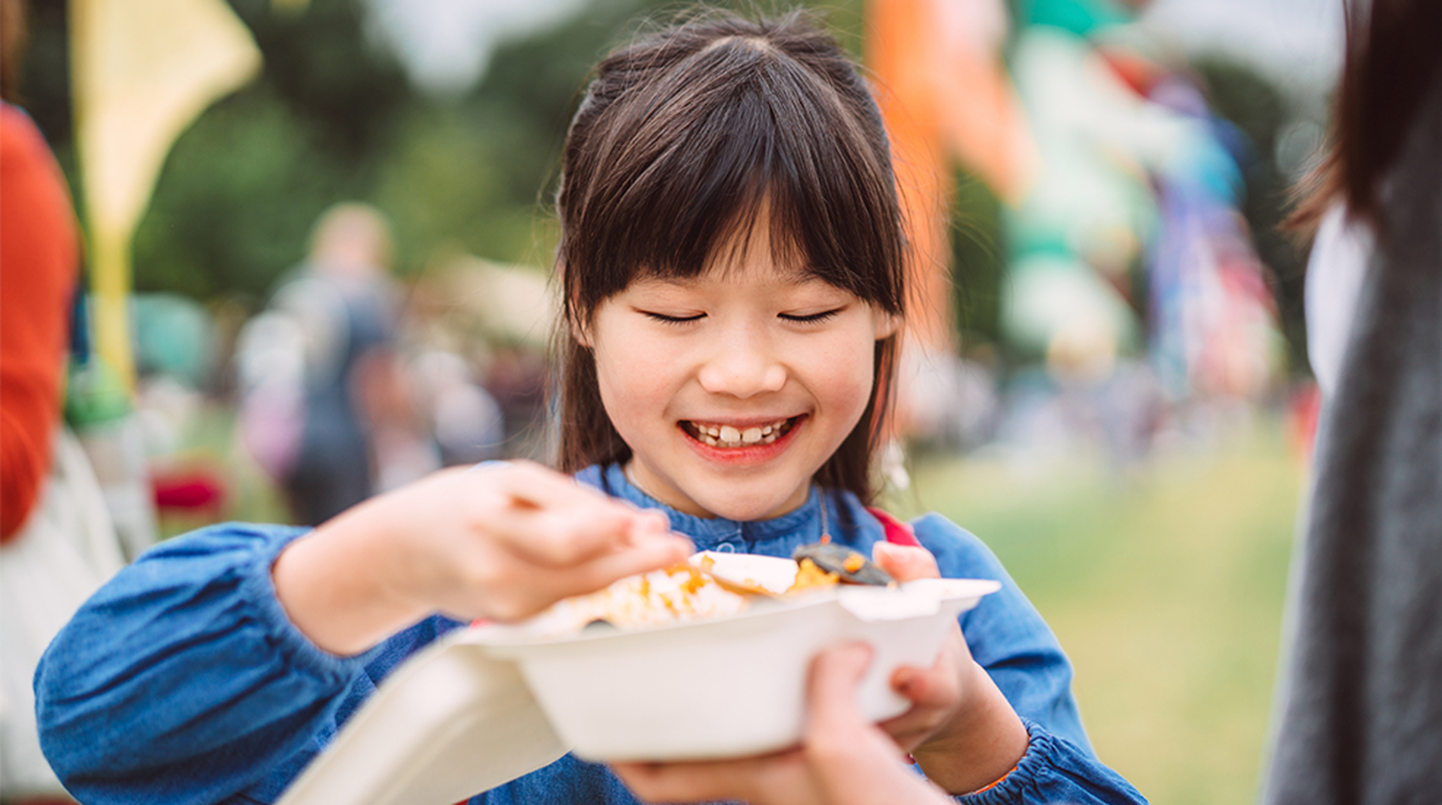 Happy Asian child eating street food at outdoor festival